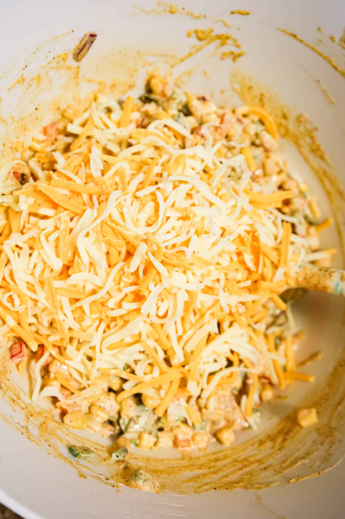 shredded cheese on top of corn salad mixture in a mixing bowl