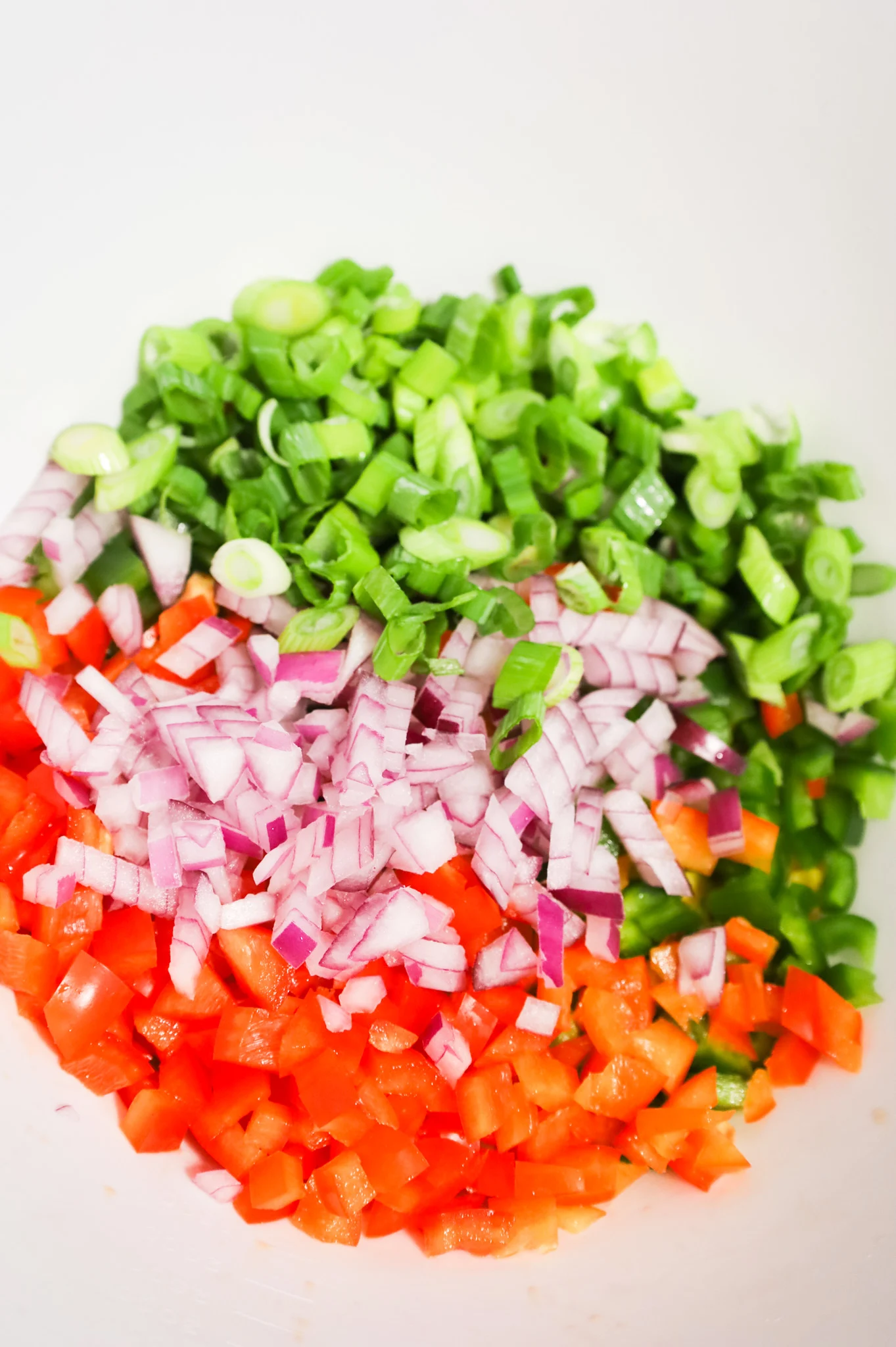 chopped green onions, diced red onions, diced red bell peppers and diced green bell peppers in a mixing bowl