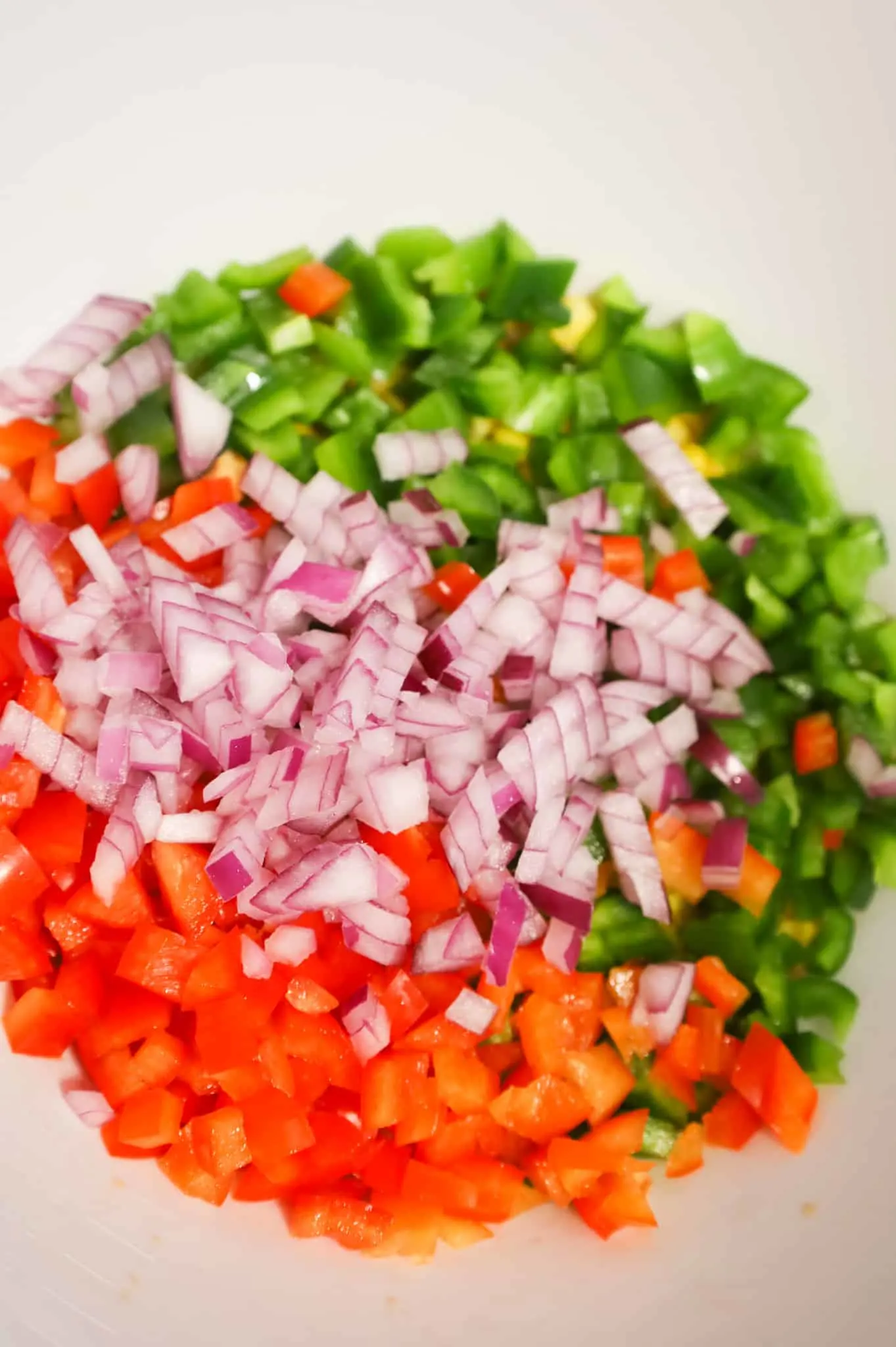 diced red onions, red bell peppers and green bell peppers in a mixing bowl