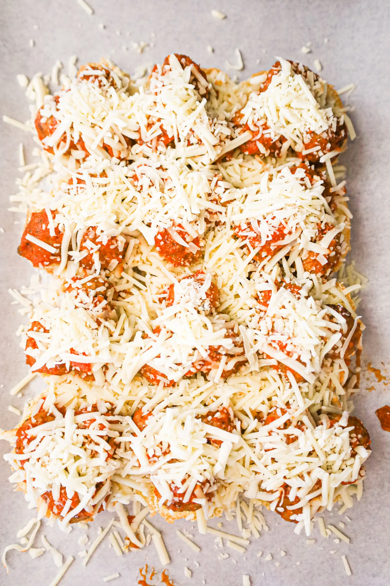 shredded cheese and meatballs on buns on a baking sheet