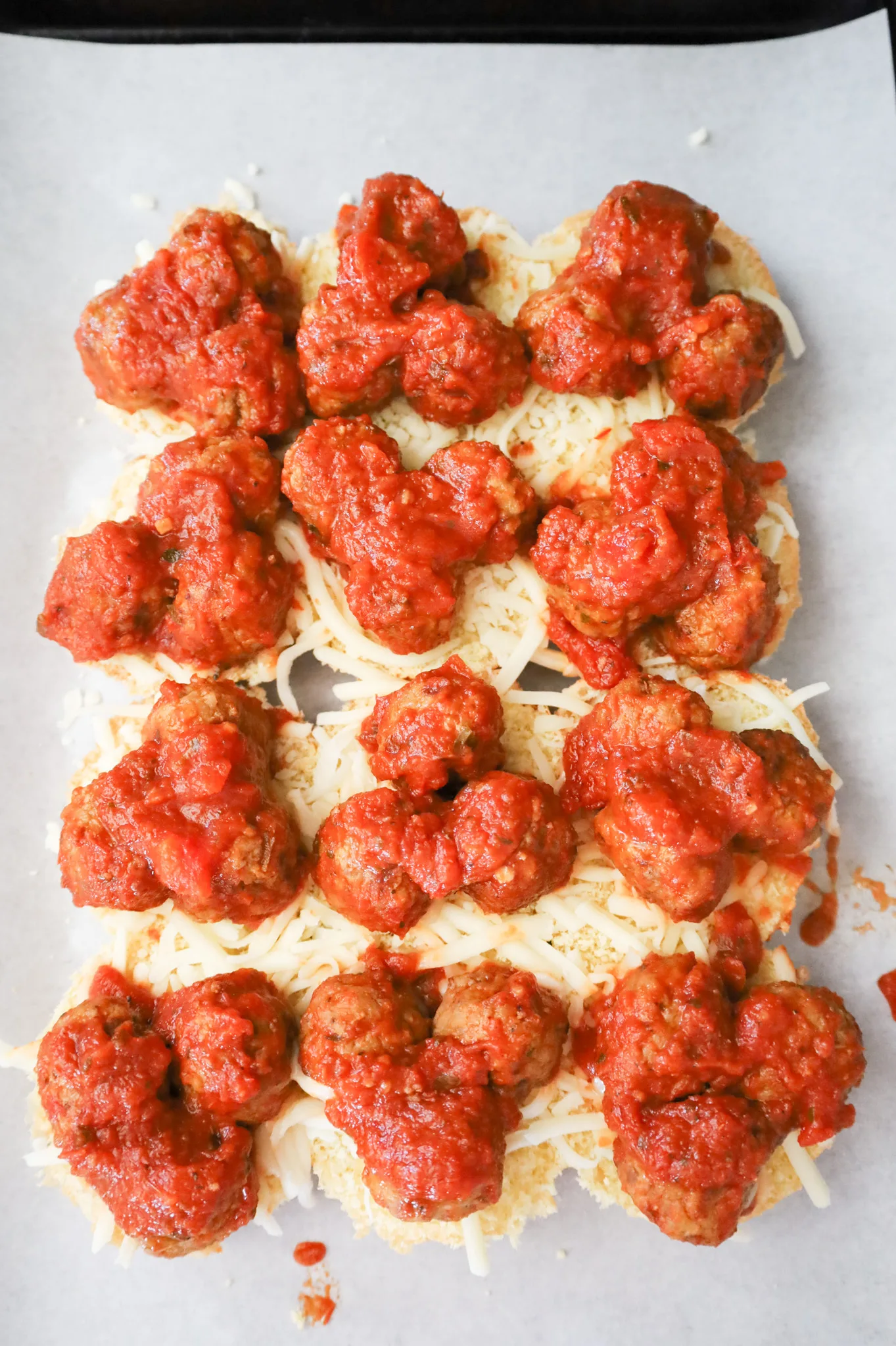 meatballs and shredded cheese on top of dinner rolls on a baking sheet