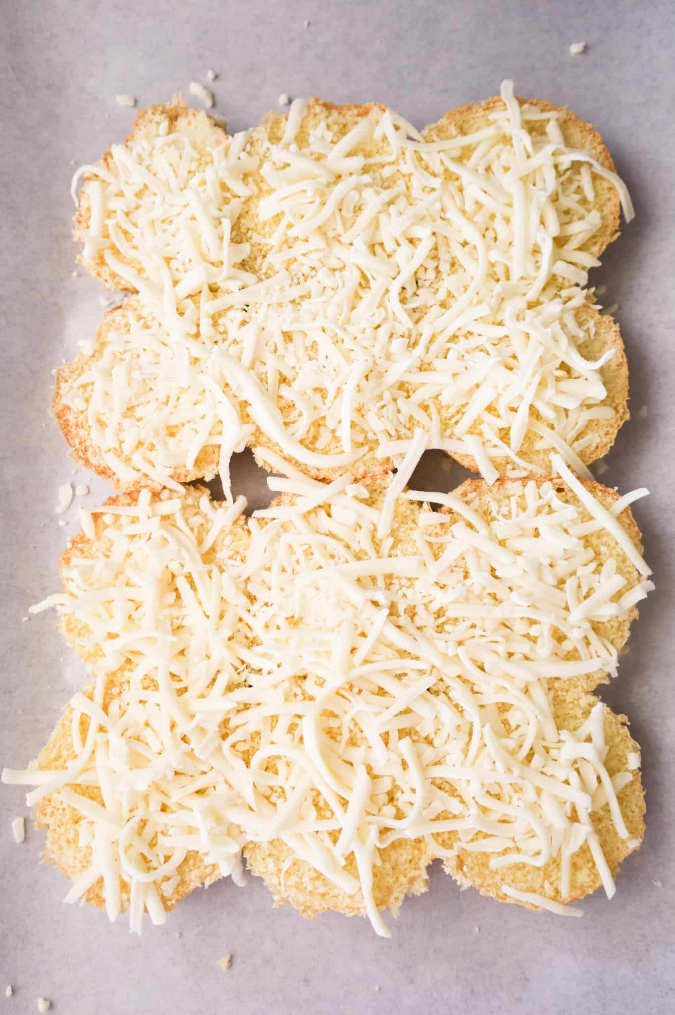 shredded mozzarella on buns on a baking sheet