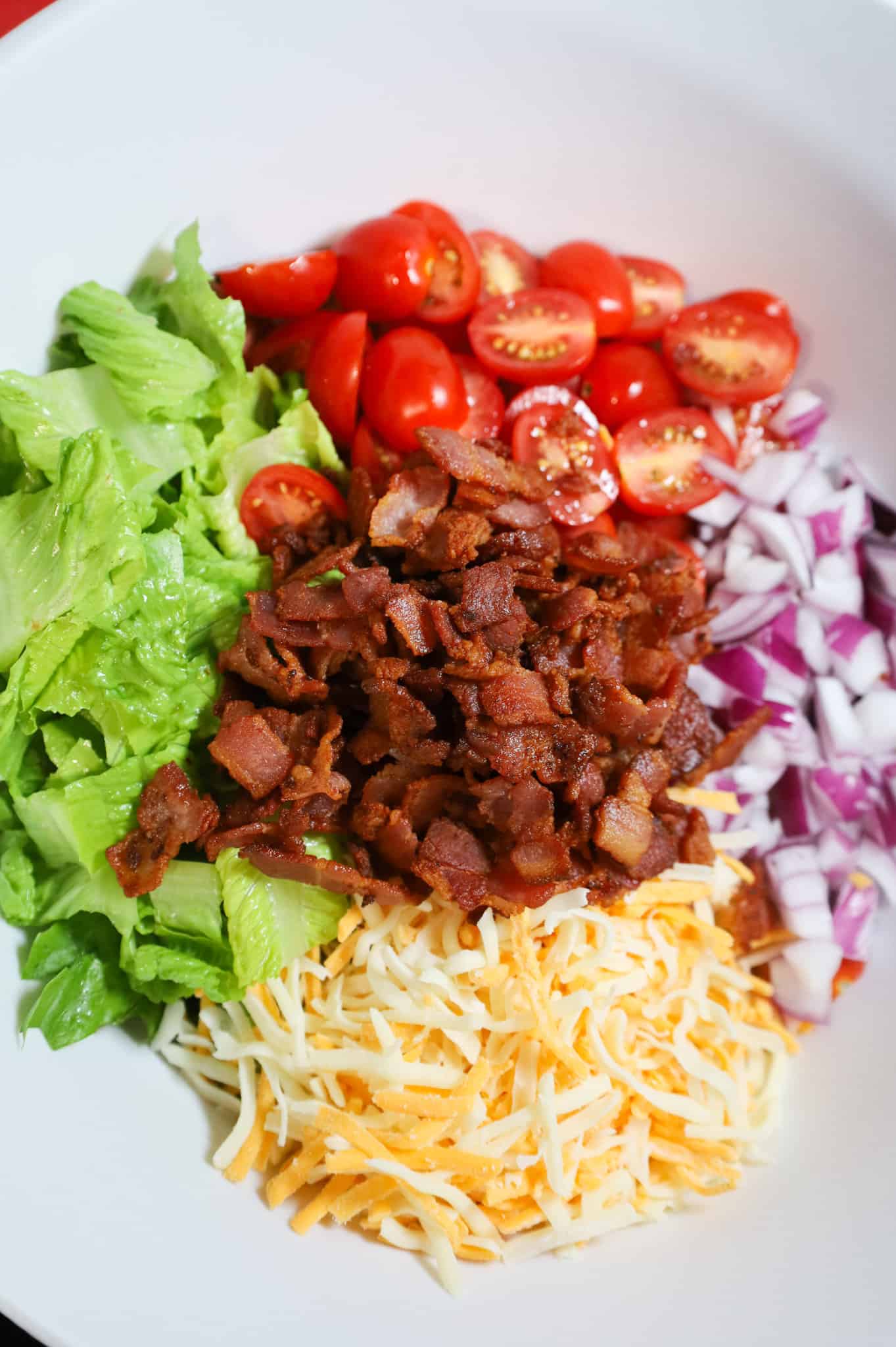cooked bacon pieces, chopped romaine, diced red onions, grape tomatoes and shredded cheese in a mixing bowl