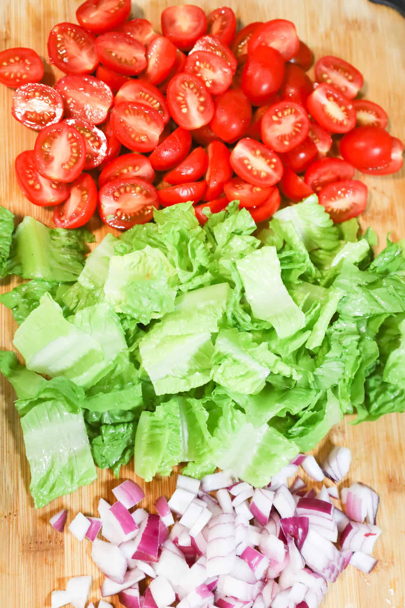 halved grape tomatoes, chopped romaine lettuce and diced red onions on a cutting board
