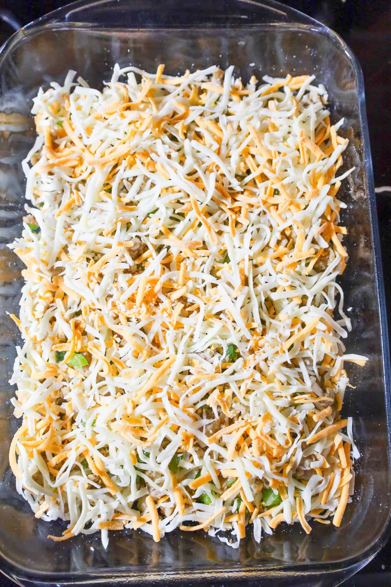 shredded cheese on top of sausage and biscuits in a baking dish