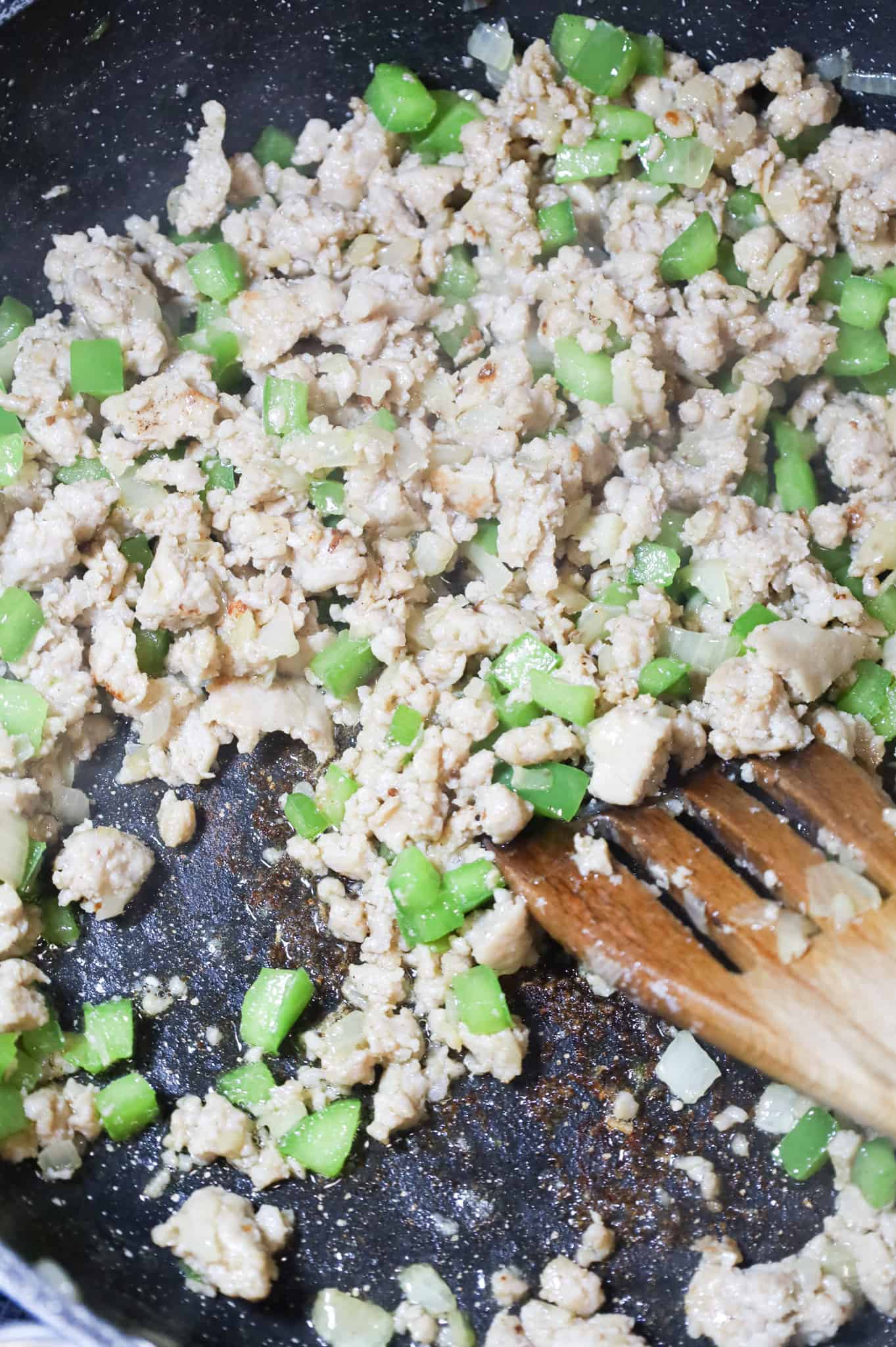 ground sausage and diced green peppers being stirred while cooking in a skillet
