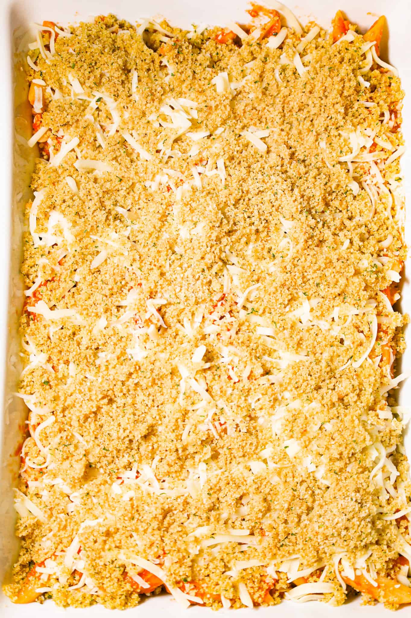 bread crumb mixture sprinkled on top of shredded cheese and pasta in a baking dish