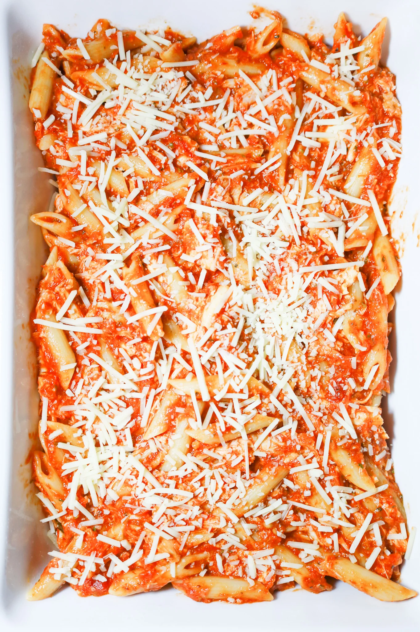 shredded parmesan cheese on top of penne marinara in a baking dish