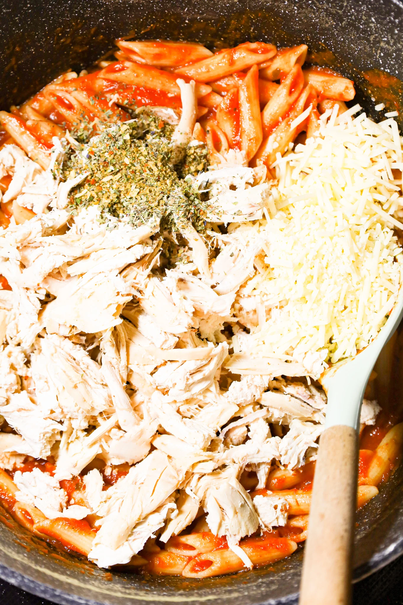 shredded chicken, Italian seasoning and shredded parmesan cheese on top of penne marinara in a large pot