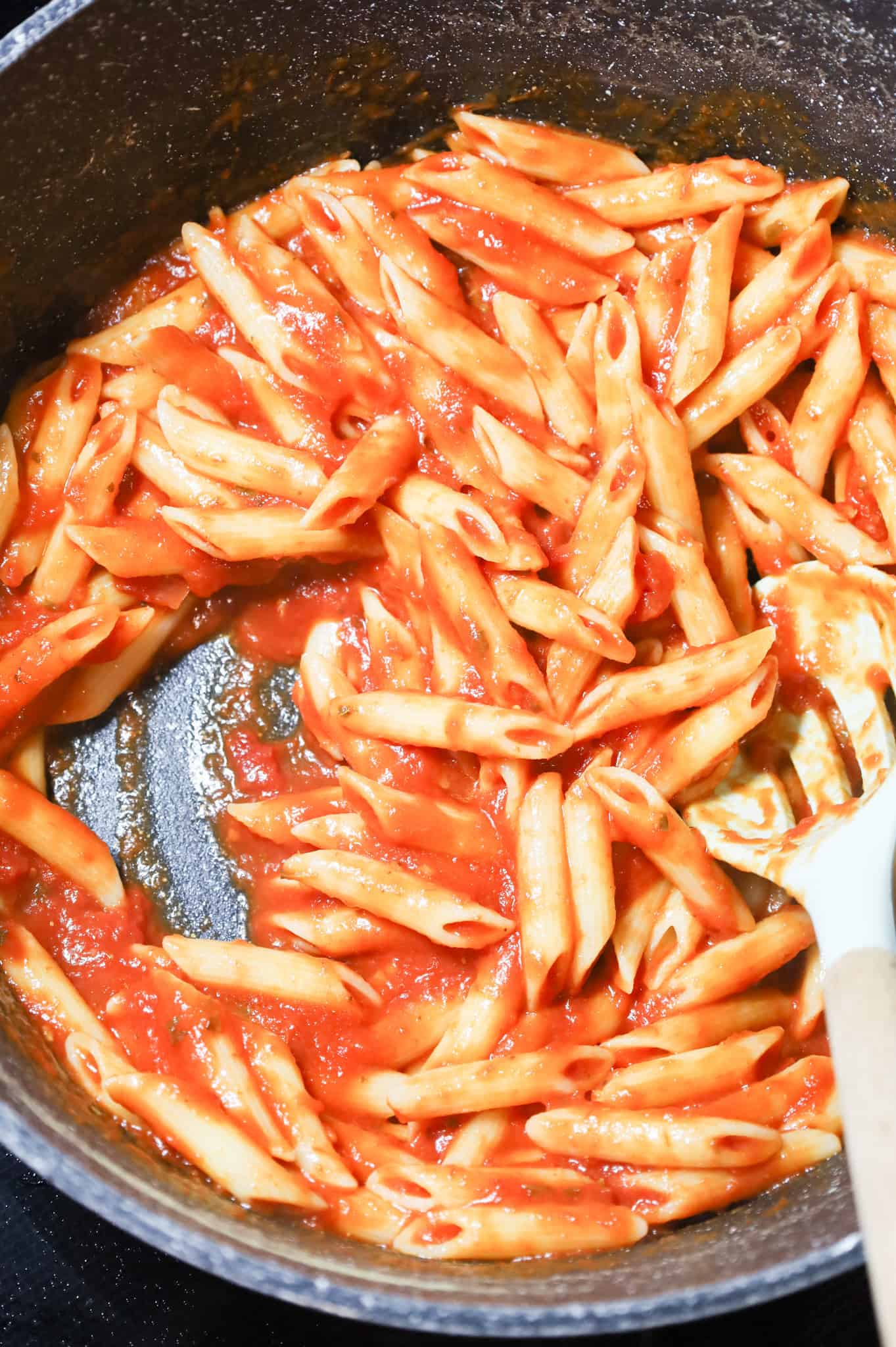 penne and marinara sauce being stirred together in a large pot