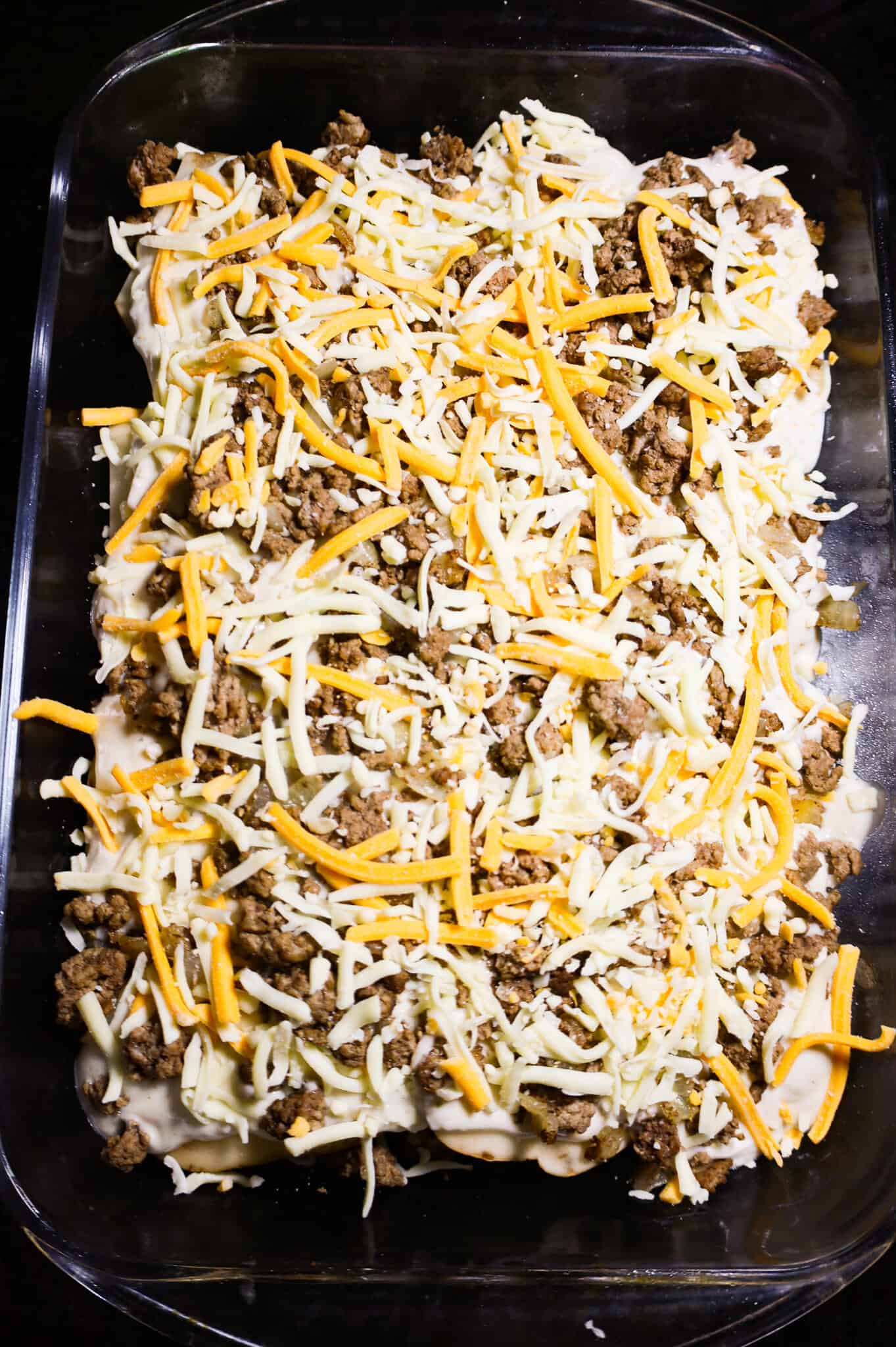 shredded cheese and crumbled ground beef on top of potatoes in a baking dish