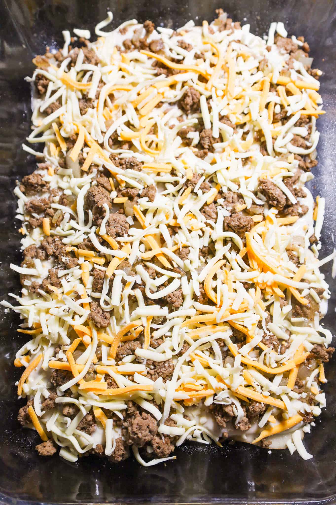 ground beef and shredded cheese on top of sliced potatoes in a baking dish