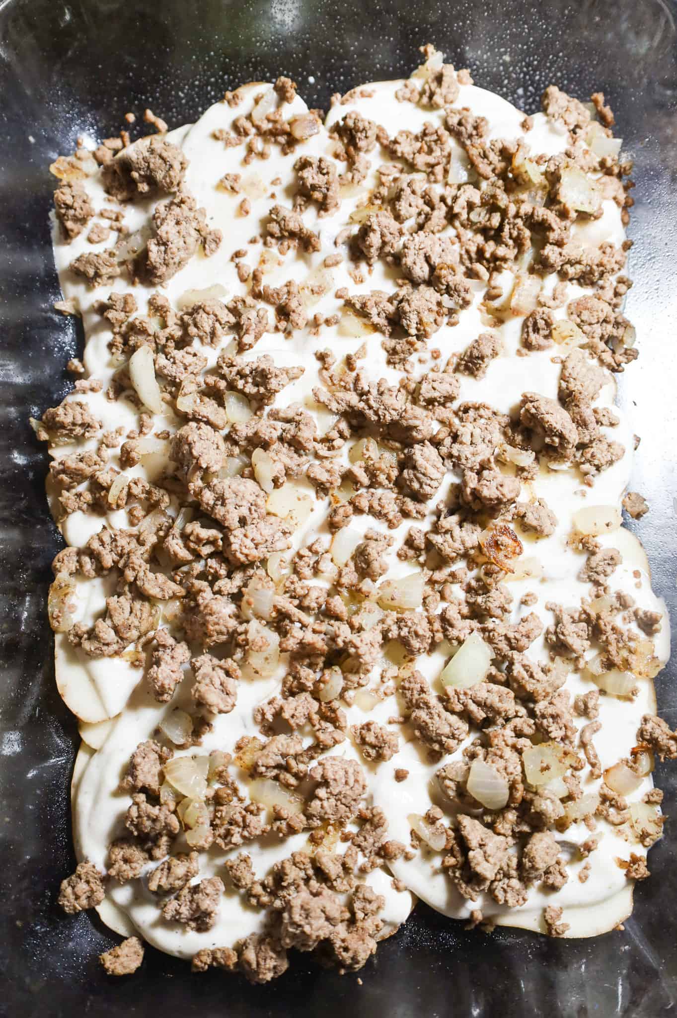 crumbled ground beef and mushrooms soup mixture on top of potatoes in a baking dish