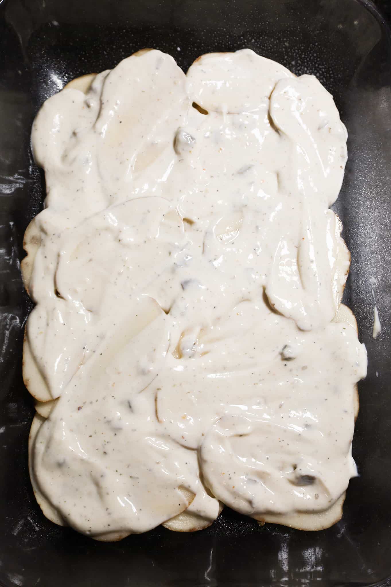 mushroom soup mixture spread on top of sliced potatoes in a baking dish