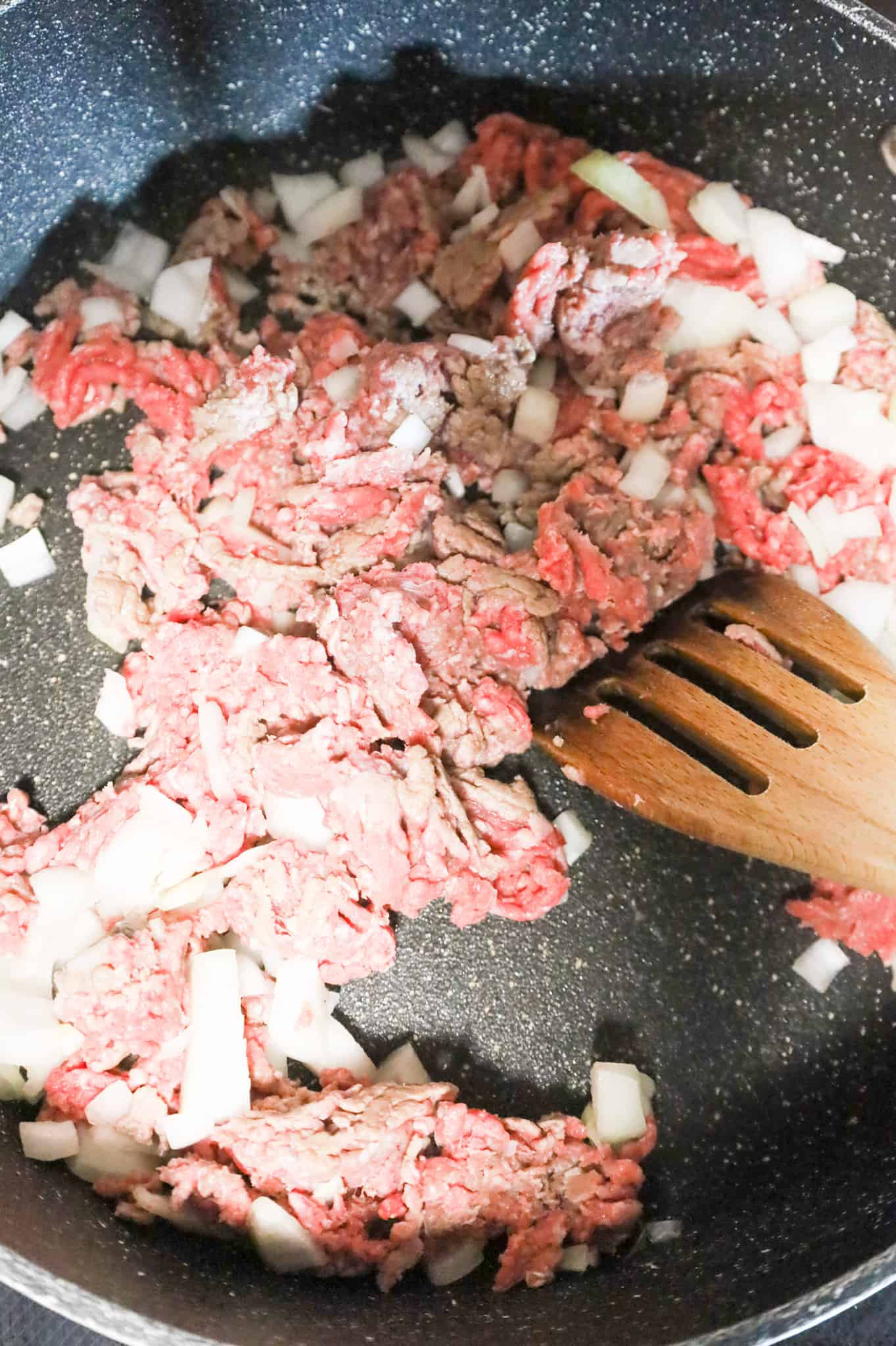 ground beef and diced onions cooking in a skillet