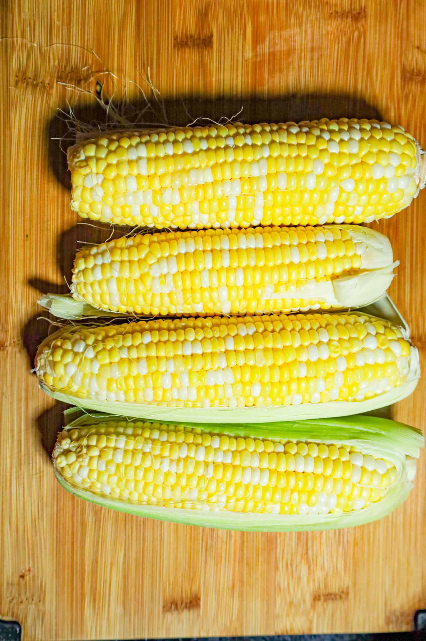corn cobs with partial husks on a cutting board