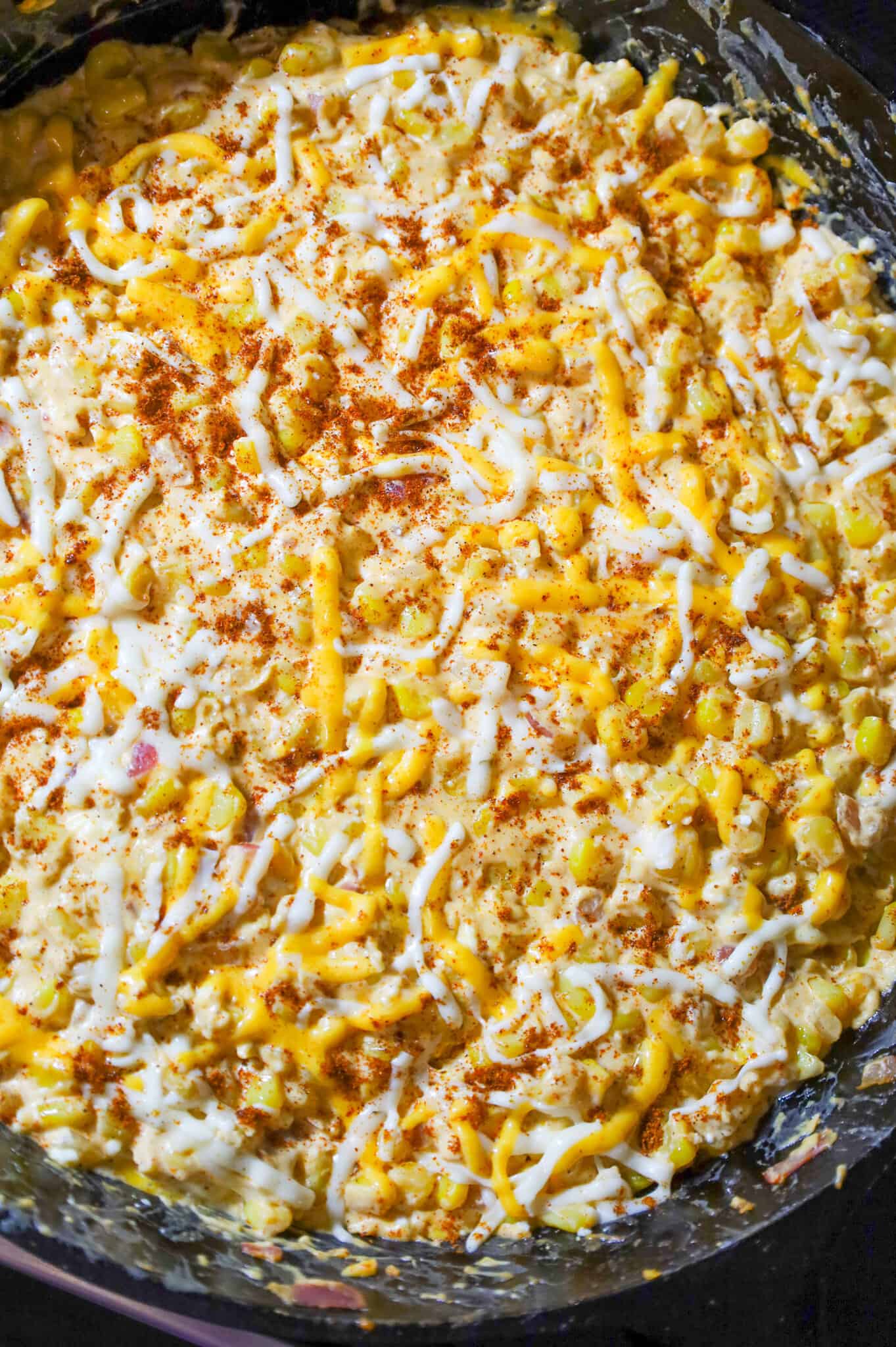 shredded cheese and chili powder on top of creamy corn mixture in a skillet
