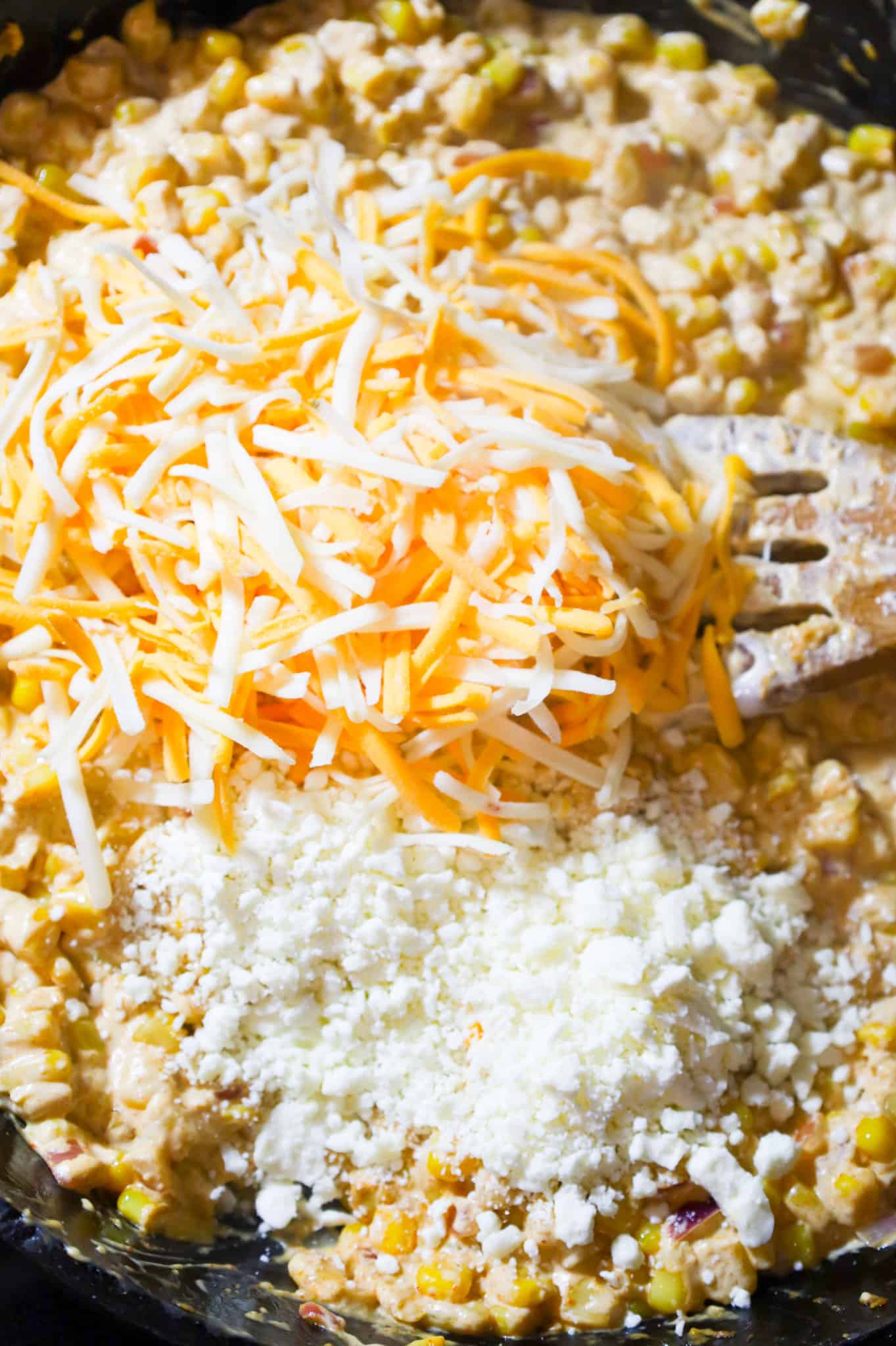 shredded cheese and crumbled feta on top of cream cheese and corn mixture in a skillet