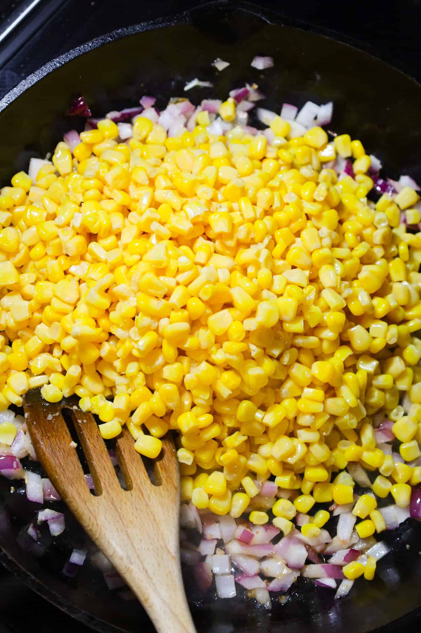 canned corn on top of diced red onion mixture in a skillet