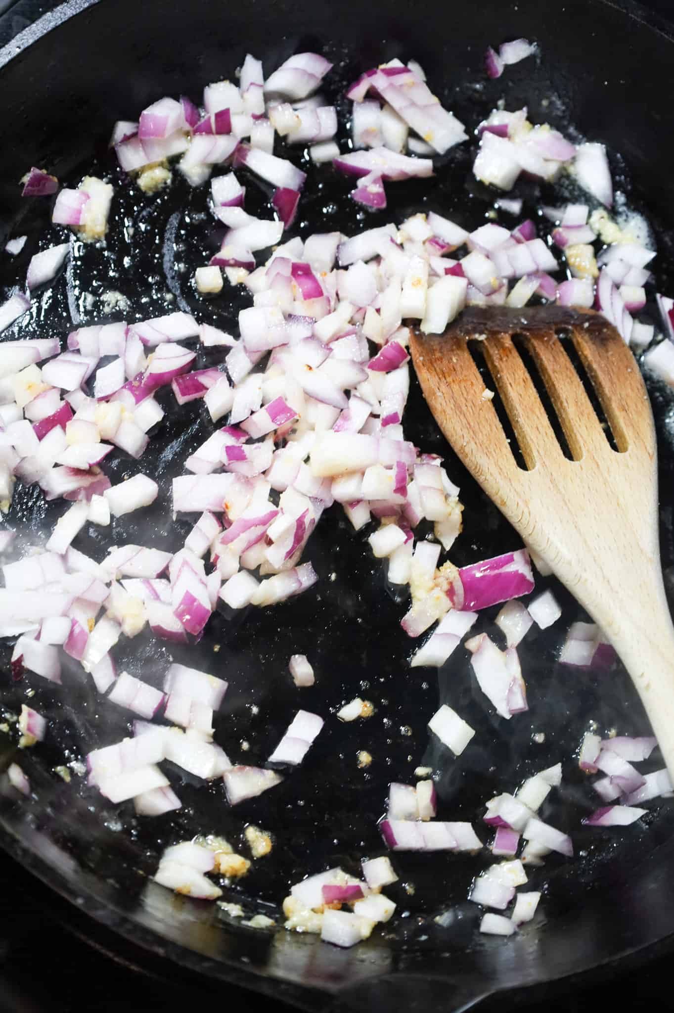 stirring together diced red onions, garlic puree and melted butter in a cast iron skillet