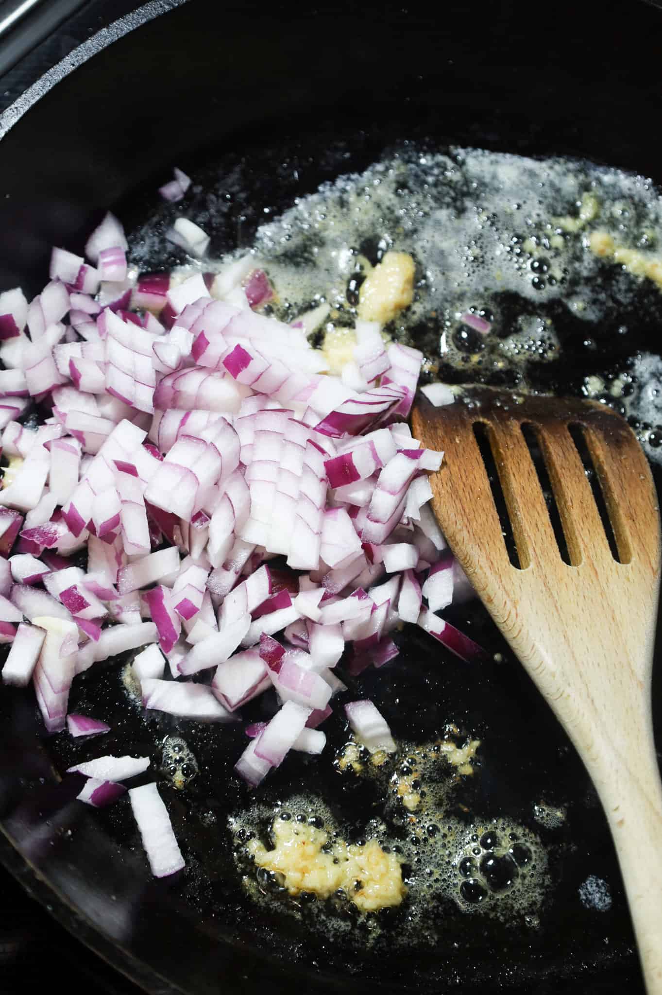 diced red onions added to a cast iron skillet with garlic puree and melted butter