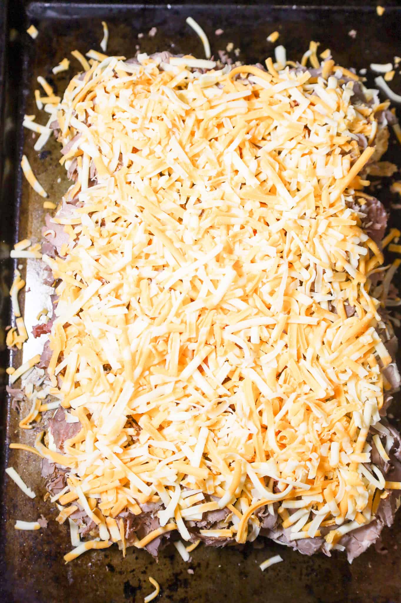 shredded mozzarella and cheddar cheese on top of roast beef buns on a baking sheet