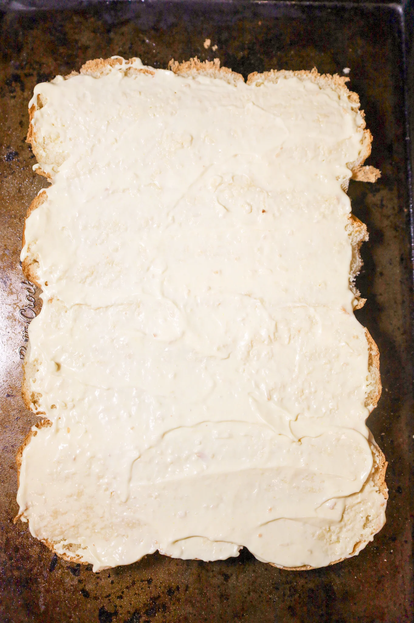 mayo and horseradish sauce mixture spread on bottom buns on a baking sheet