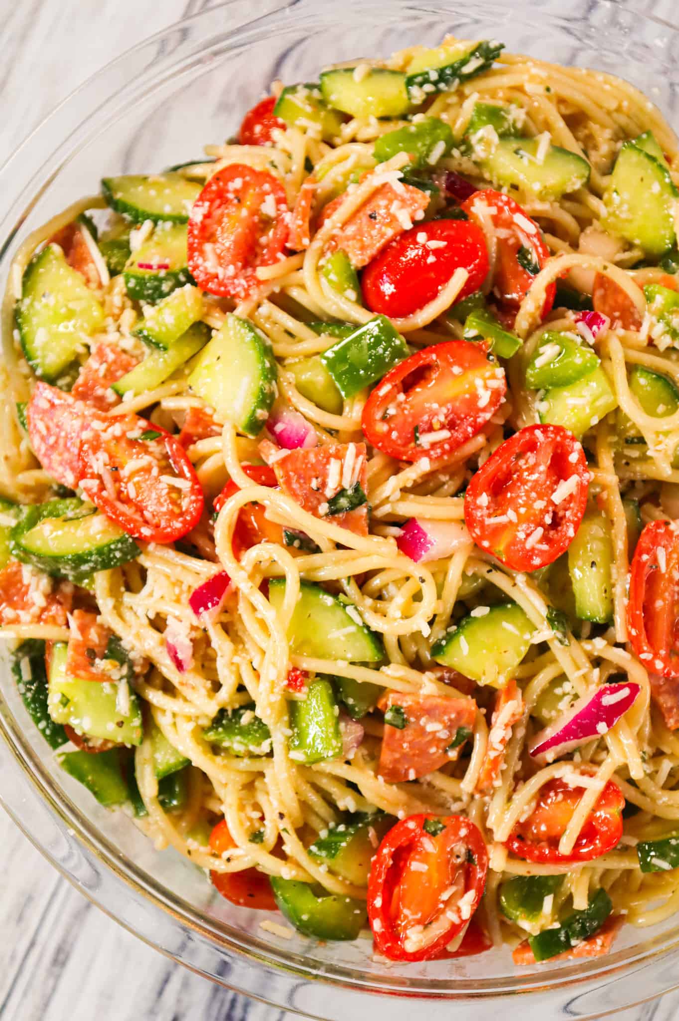 Spaghetti Salad is a tasty pasta salad recipe loaded with cucumbers, grape tomatoes, green peppers, red onions, pepperoni and grated parmesan all tossed in Italian dressing.