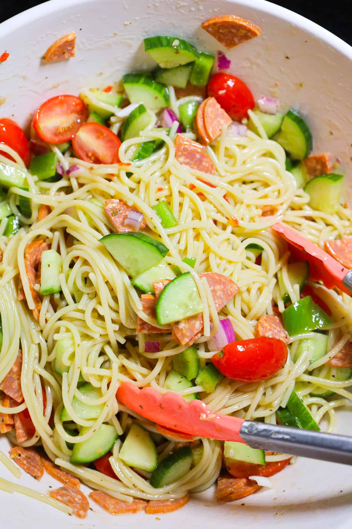 tossing spaghetti salad with veggies in a mixing bowl