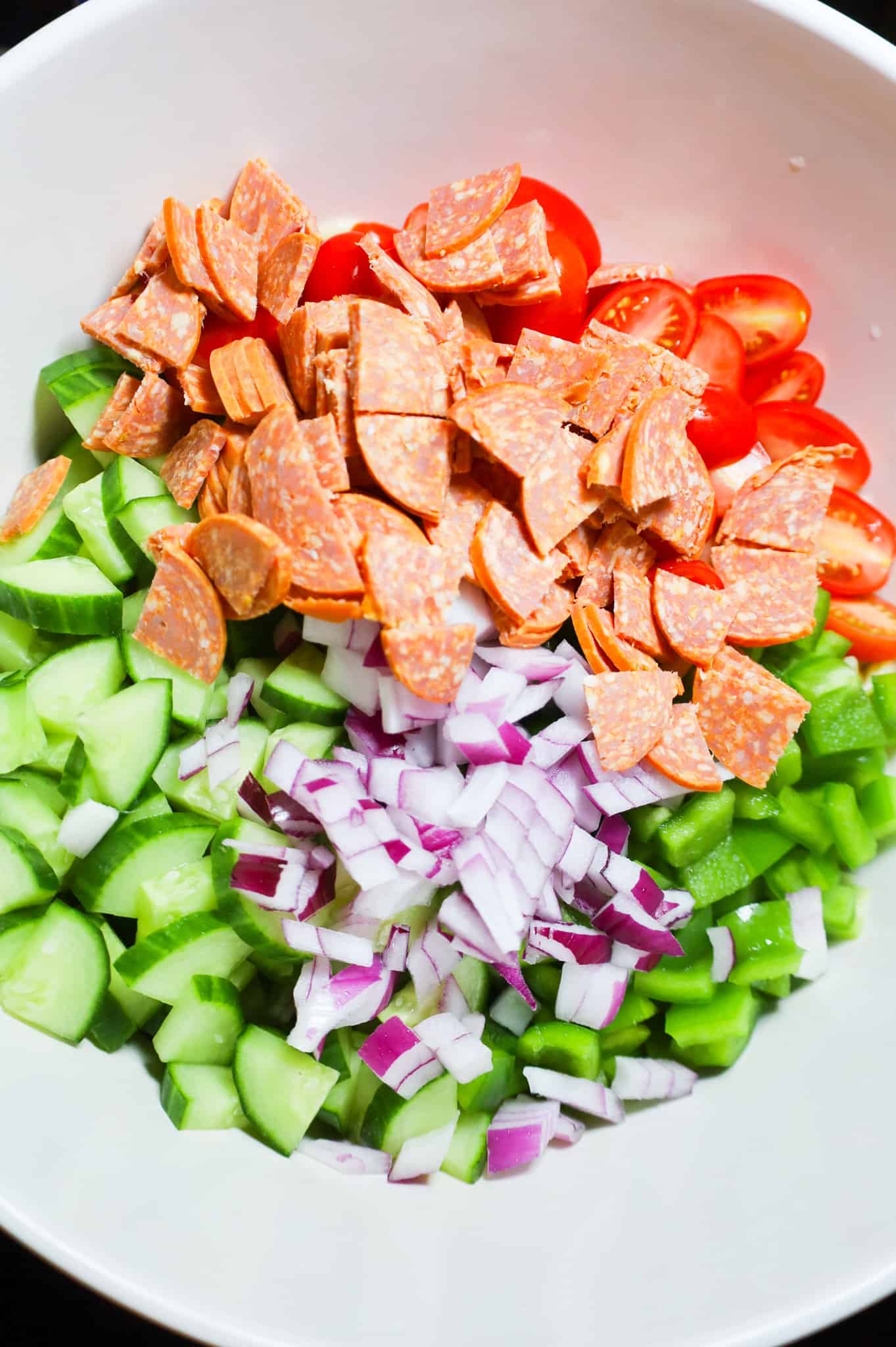 chopped pepperoni, diced red onions, diced cucumbers, diced green peppers and halved grape tomatoes in a mixing bowl