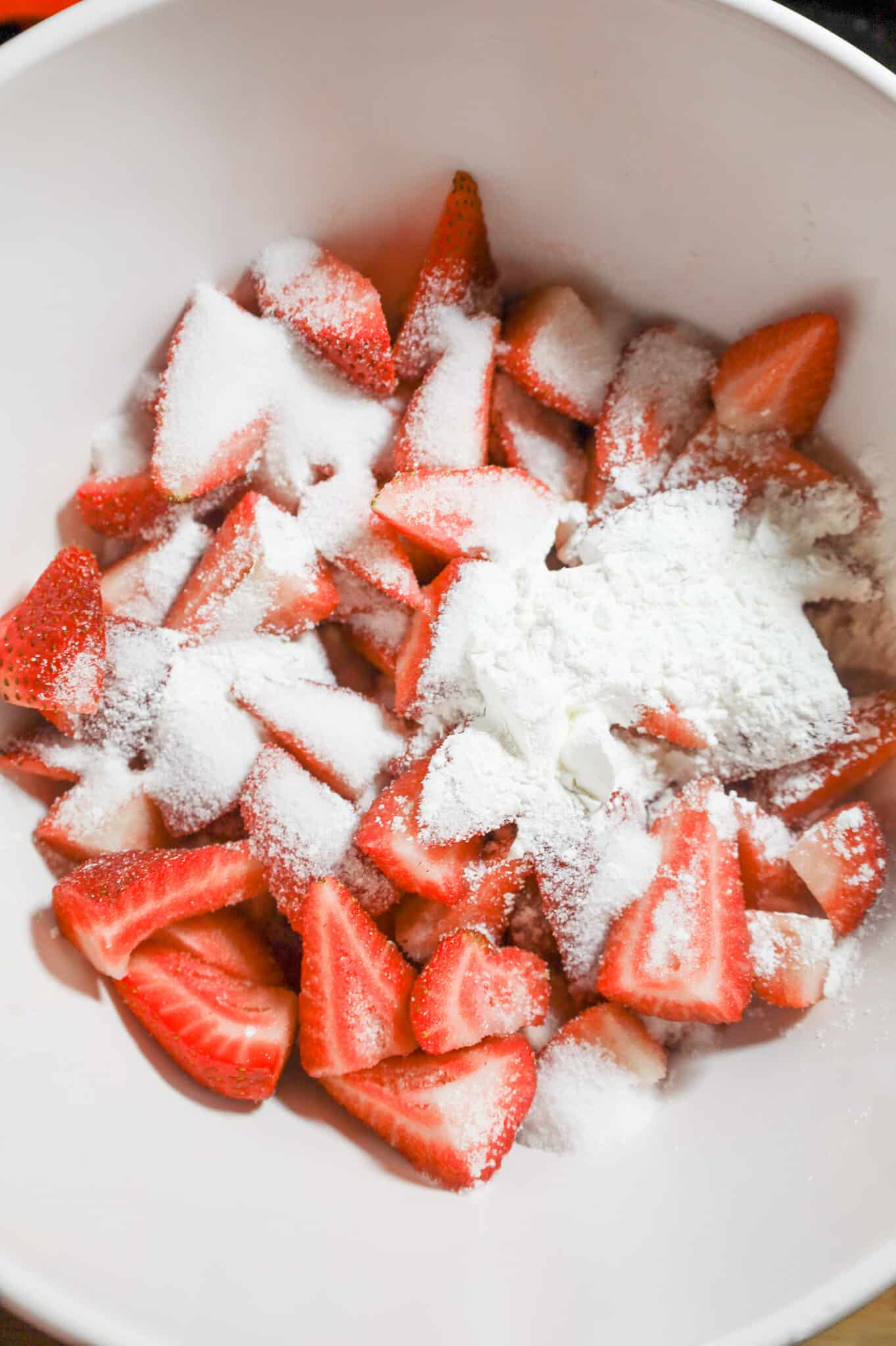 sugar and cornstarch on top of quartered strawberries in a mixing bowl