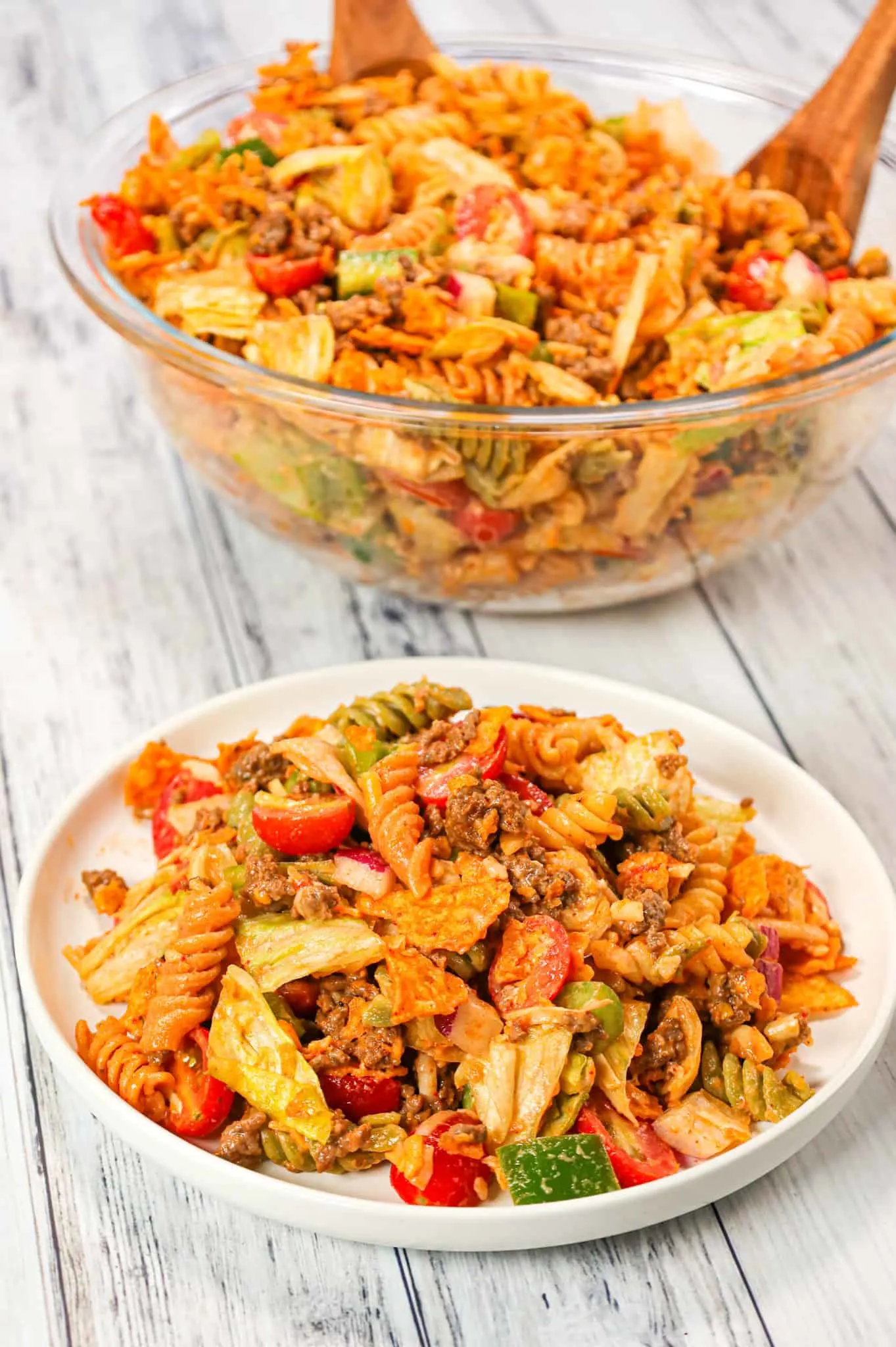 Taco Pasta Salad is the perfect party side dish loaded with tri-colour rotini pasta, taco seasoned ground beef, iceberg lettuce, onions, tomatoes, green peppers, shredded cheese, salsa, ranch dressing and crumbled Doritos nacho chips.