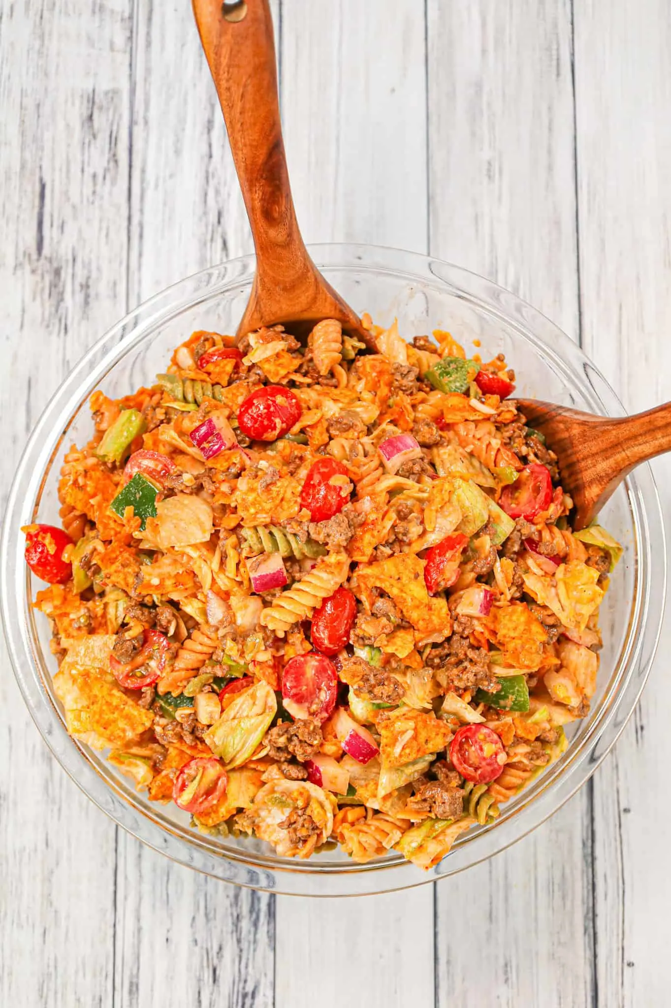 Taco Pasta Salad is the perfect party side dish loaded with tri-colour rotini pasta, taco seasoned ground beef, iceberg lettuce, onions, tomatoes, green peppers, shredded cheese, salsa, ranch dressing and crumbled Doritos nacho chips.