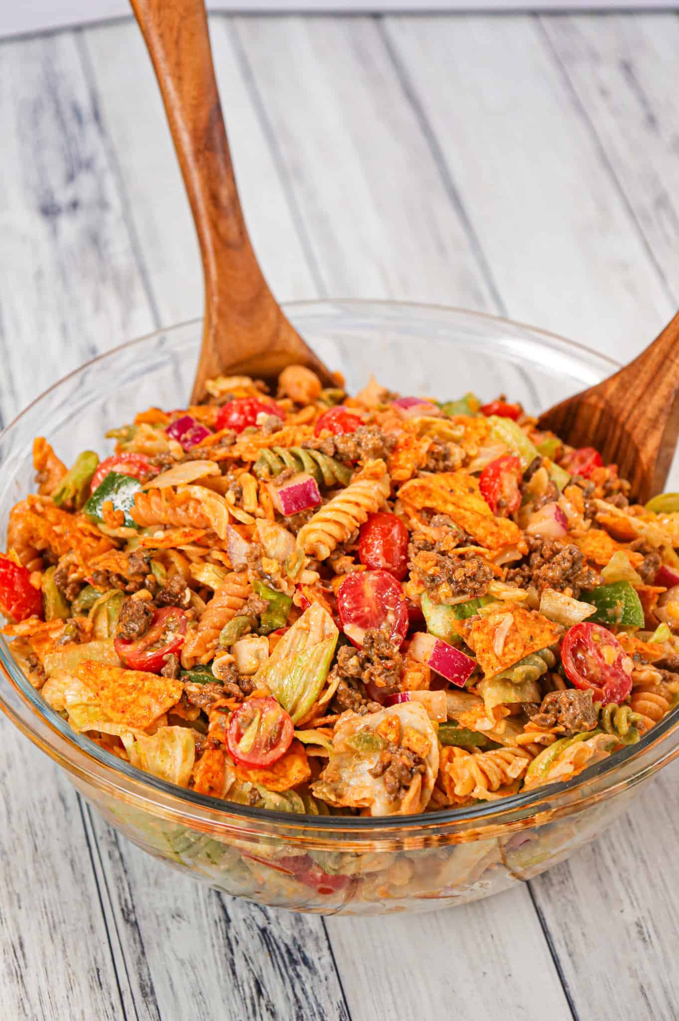 Taco Pasta Salad is the perfect party side dish loaded with tri-colour rotini pasta, taco seasoned ground beef, iceberg lettuce, onions, tomatoes, green peppers, shredded cheese, salsa, ranch dressing and crumbled Doritos nacho chips.