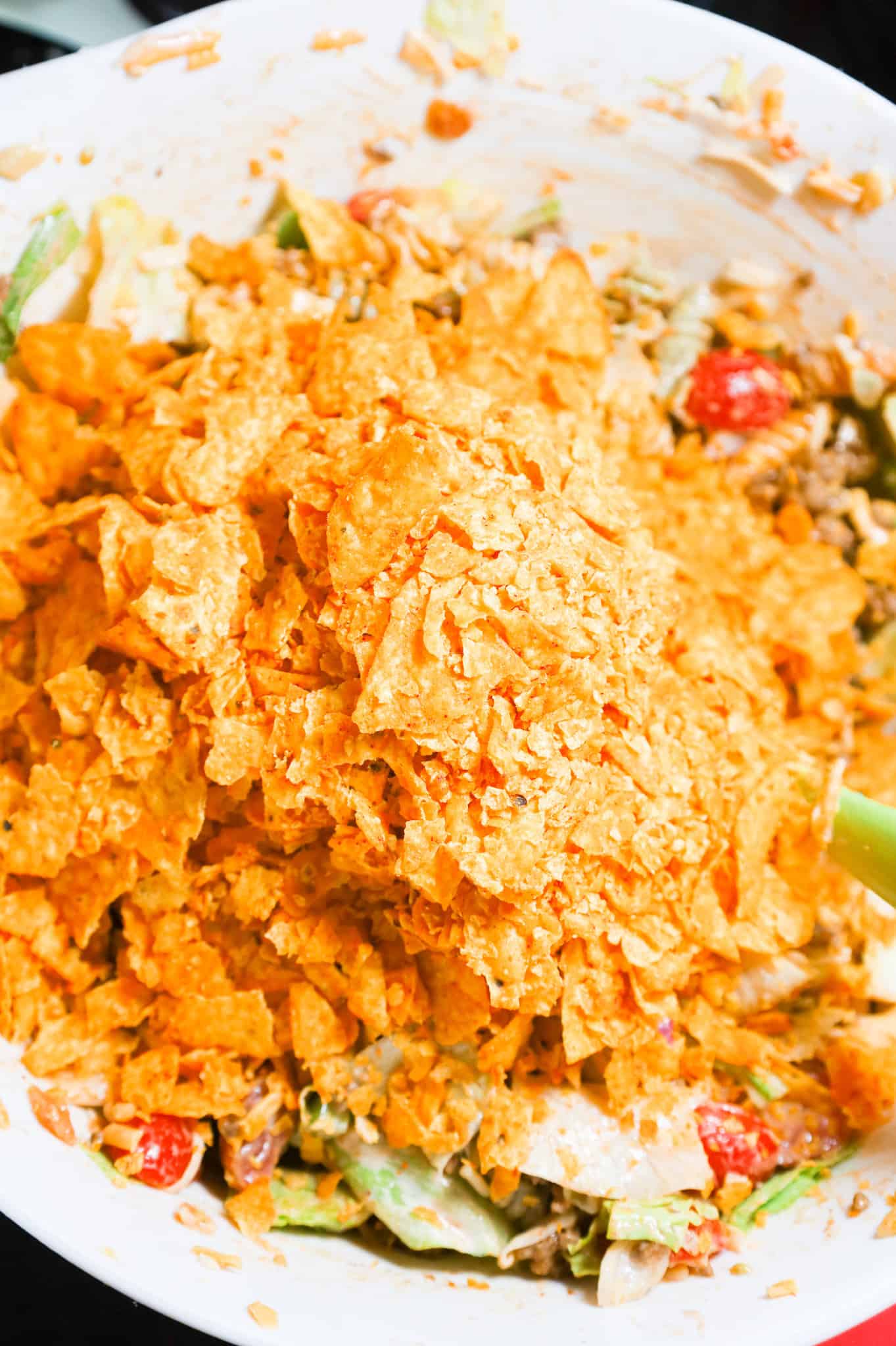 crumbled doritos on top of pasta salad in a mixing bowl