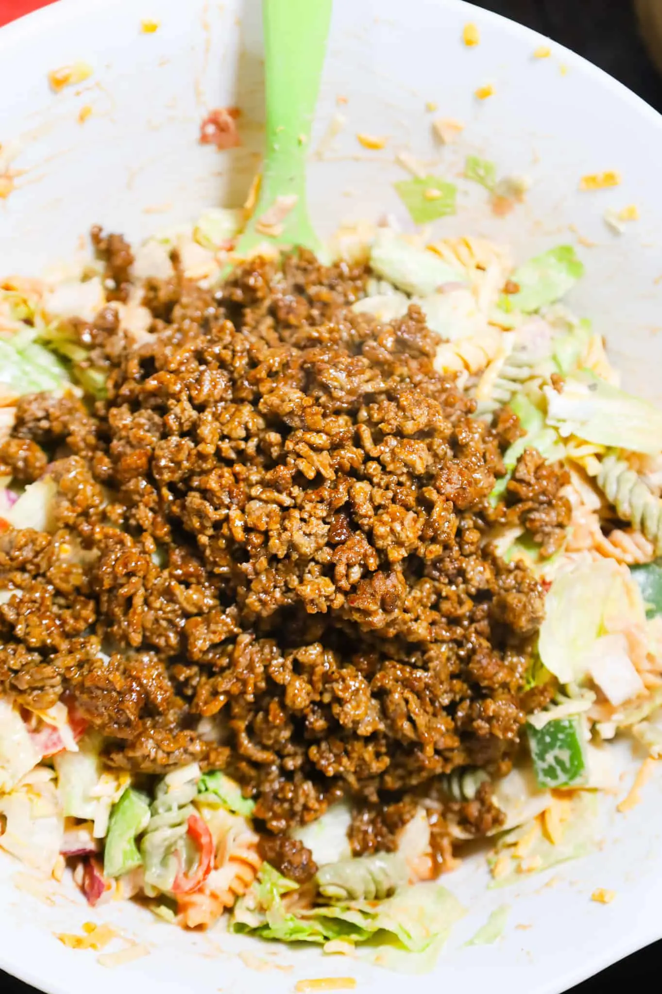 cooked ground beef taco meat added to a bowl with pasta salad mixture