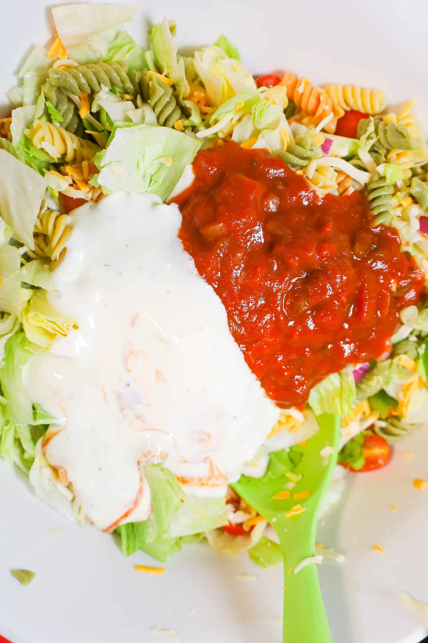 ranch dressing and salsa on top of pasta salad mixture in a mixing bowl