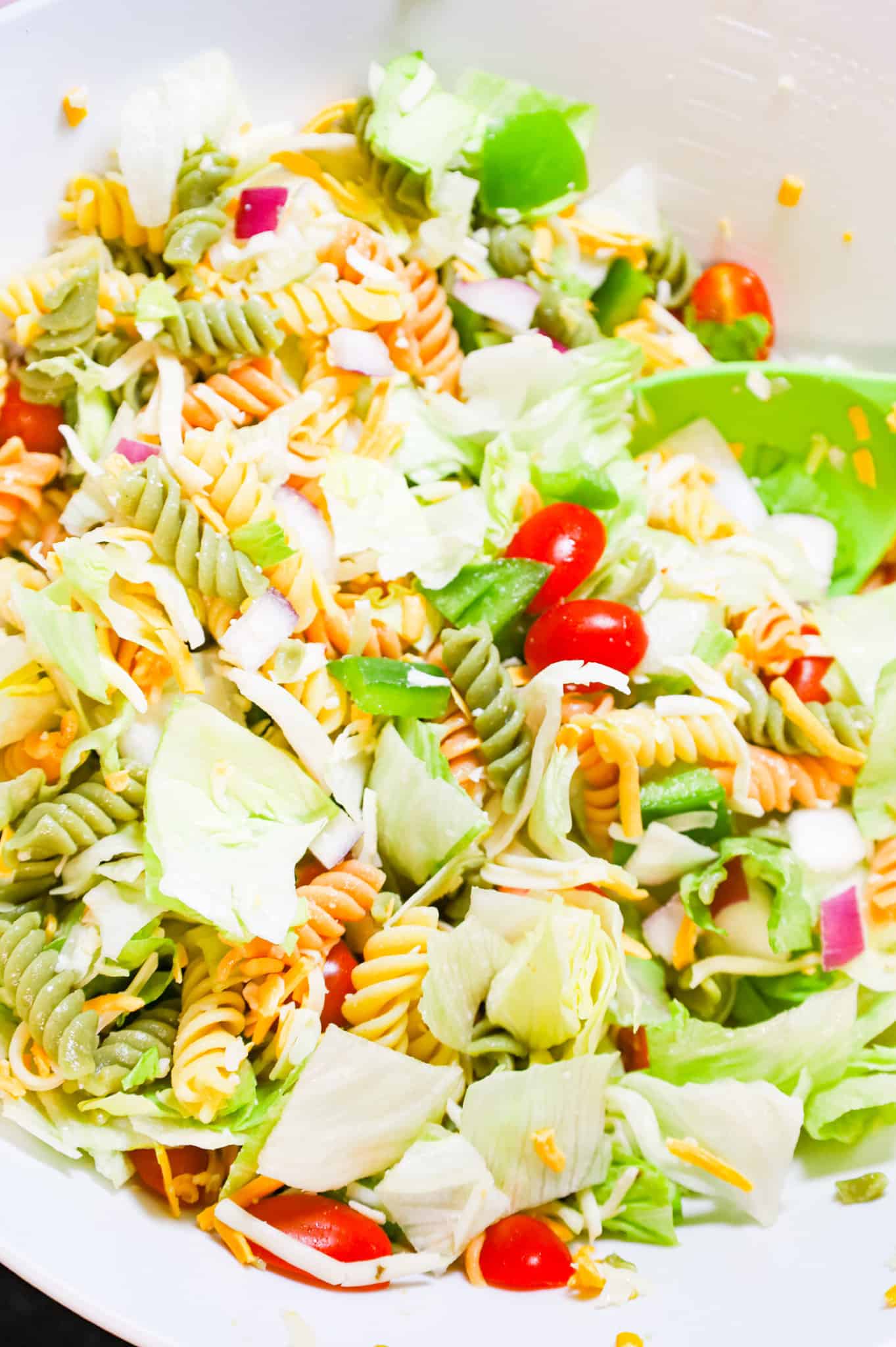 pasta salad mixture being tossed in a mixing bowl