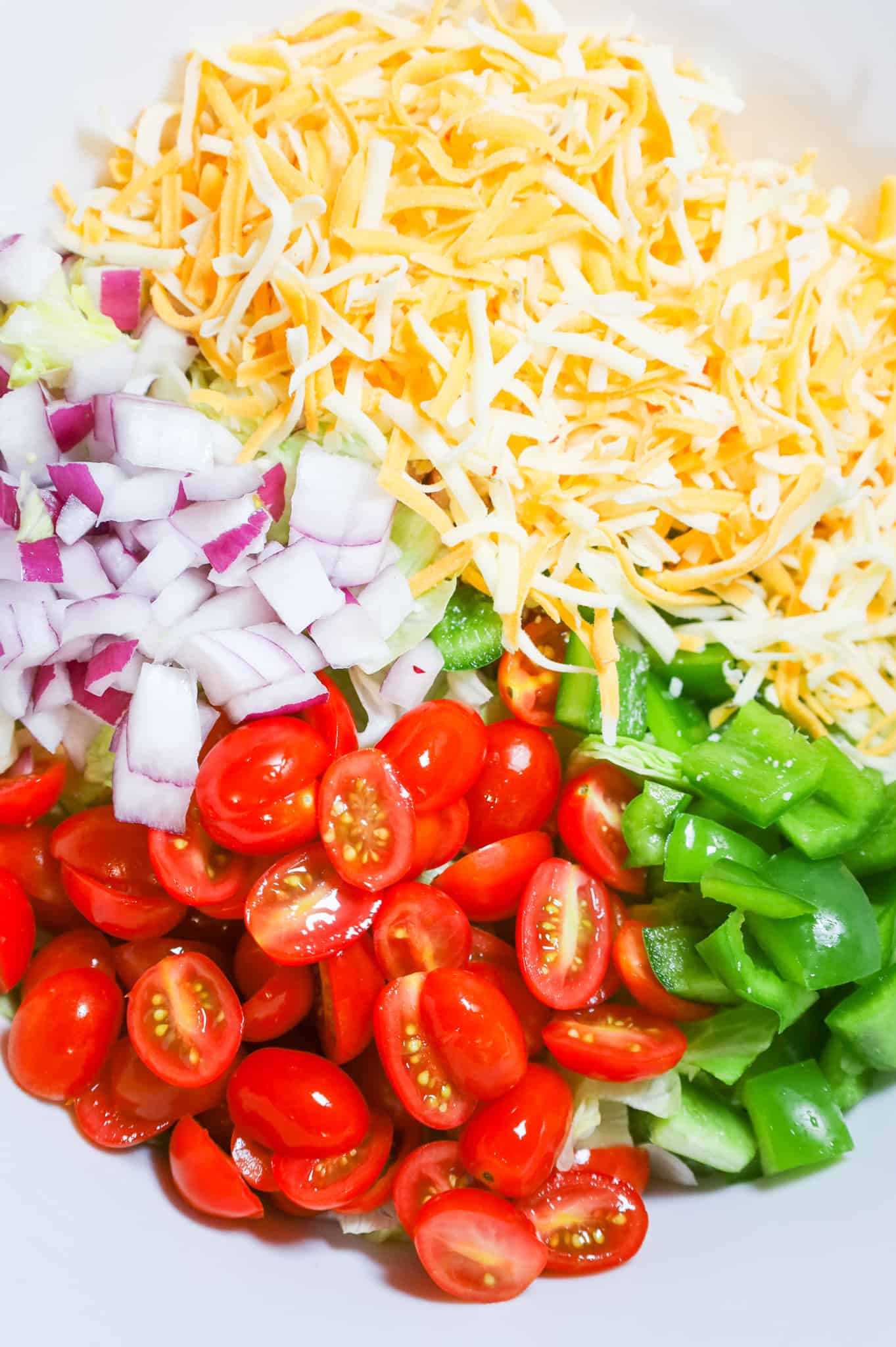 diced red onions, diced green peppers, halved grape tomatoes and shredded cheese in a mixing bowl