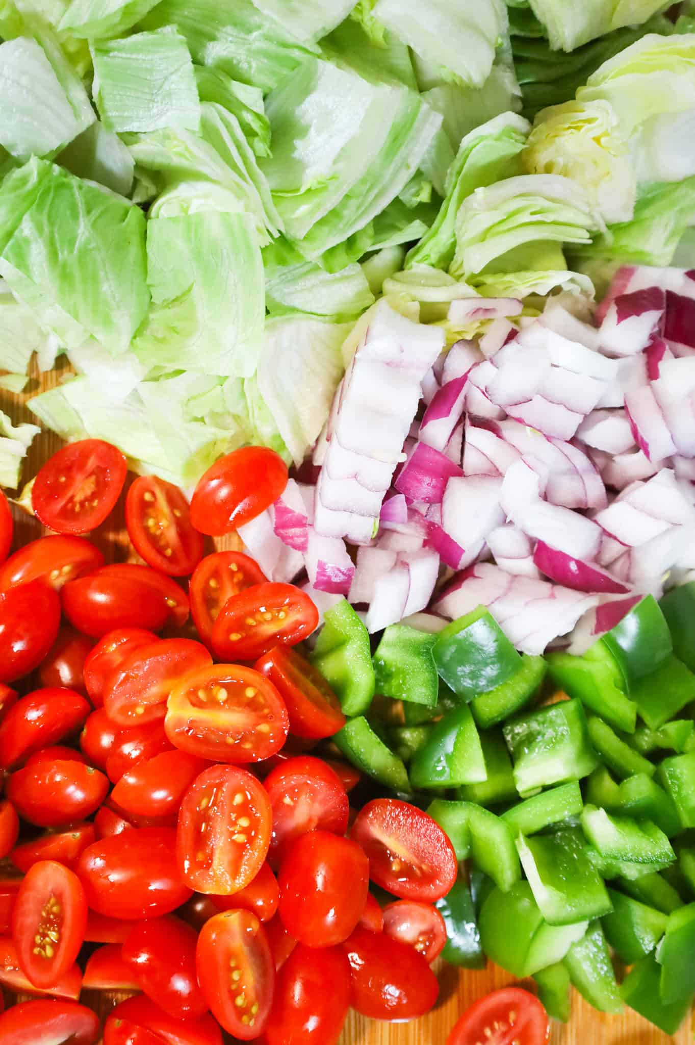 chopped lettuce, diced red onions, green peppers and halved grape tomatoes on a cutting board