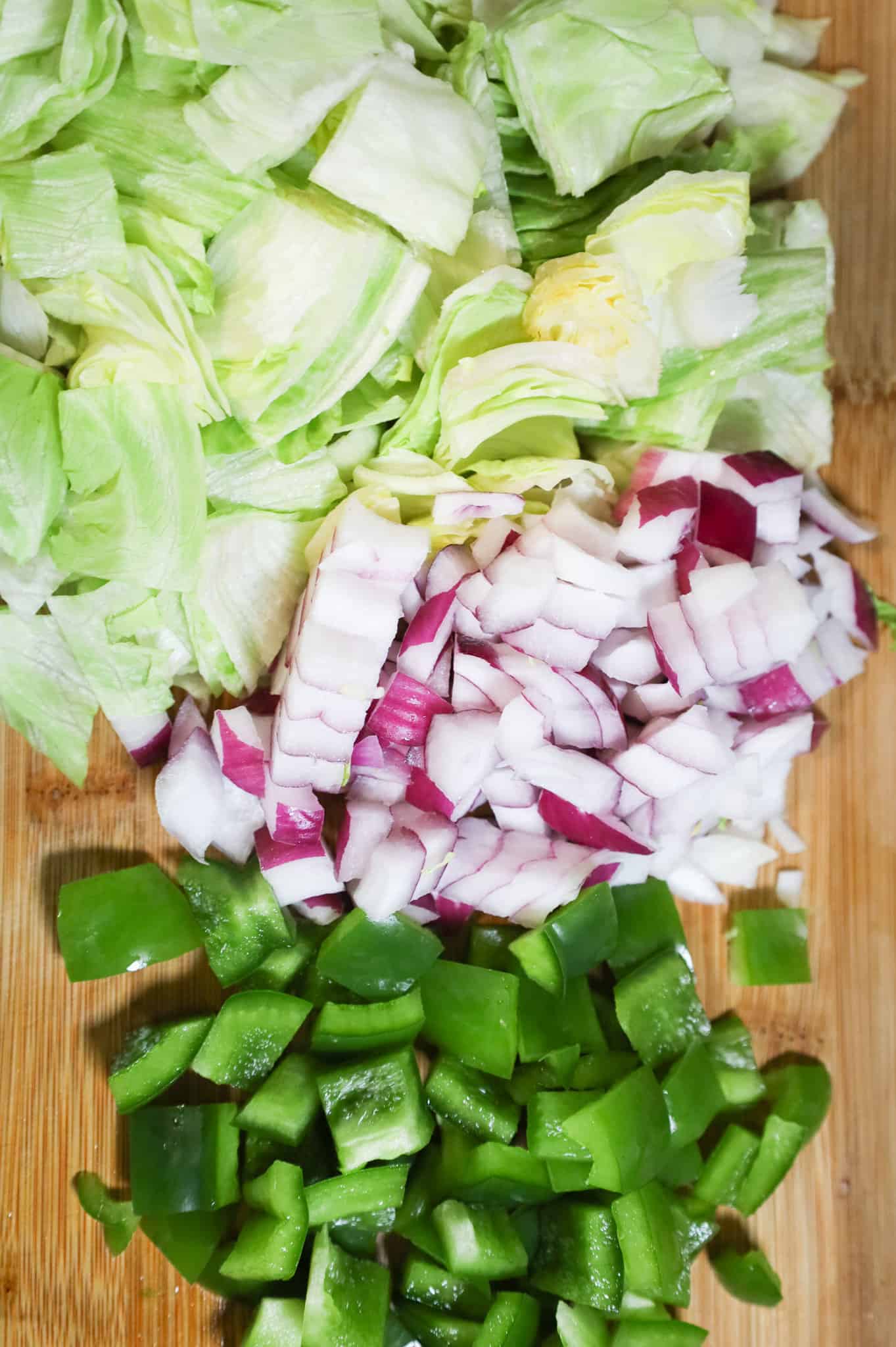 chopped iceberg lettuce and diced red onions and green peppers on a cutting board