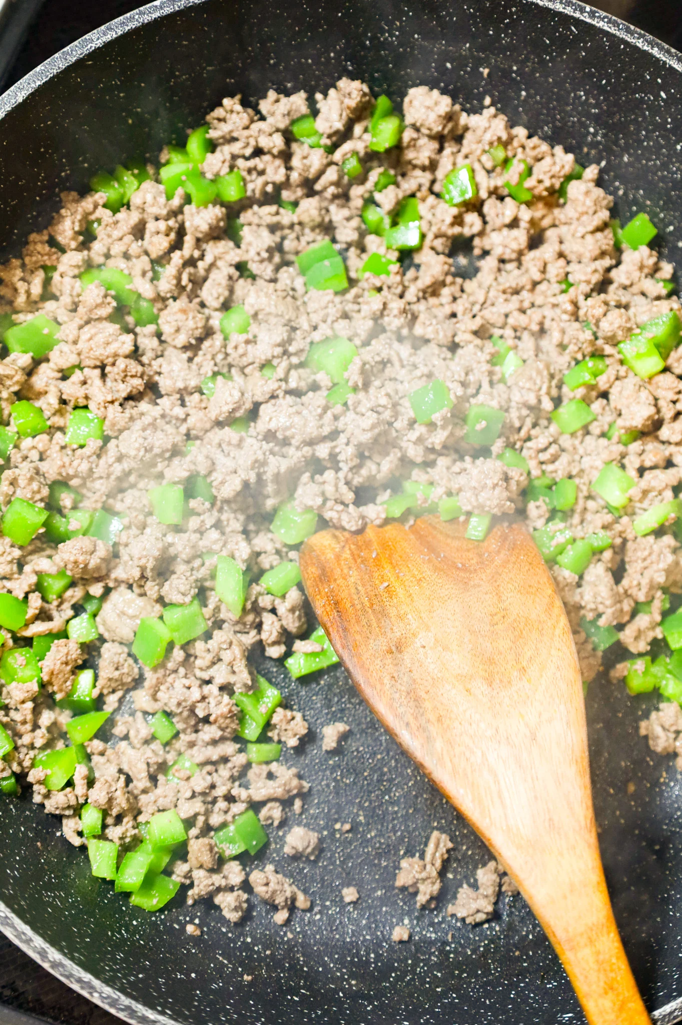 ground beef and diced green peppers cooking in a skillet
