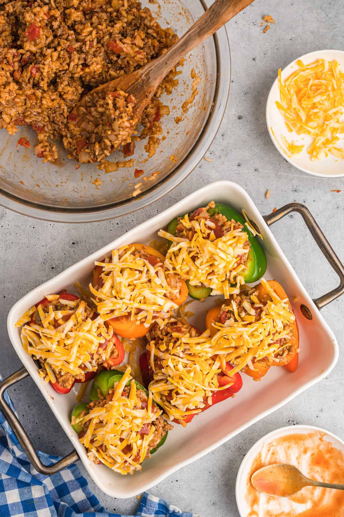 shredded cheese on top of stuffed peppers in a baking pan