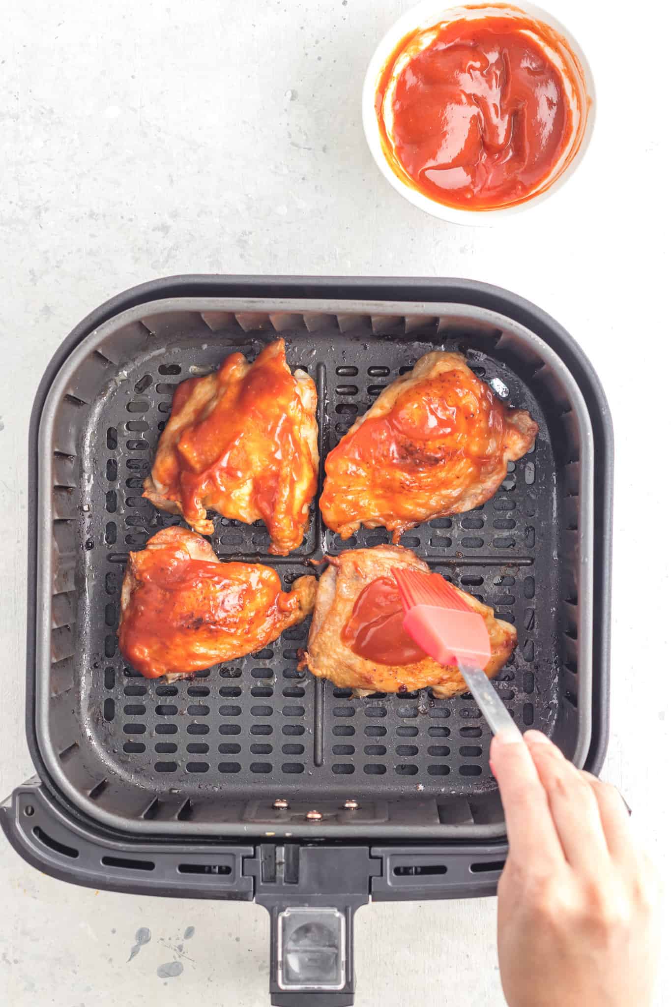 brushing bbq sauce on chicken thighs in an air fryer