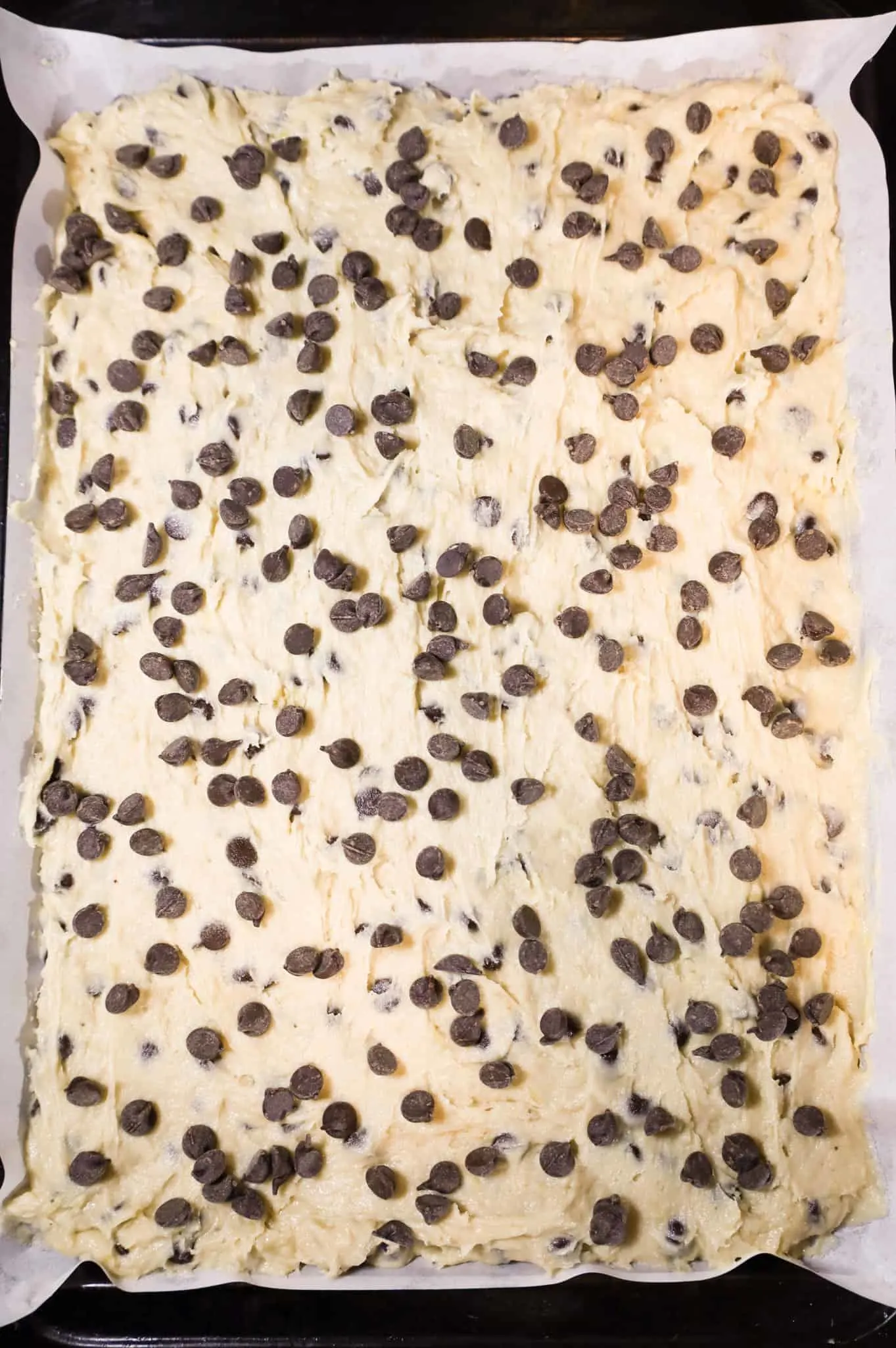 semi sweet chocolate chips on top of banana batter in a parchment lined baking sheet