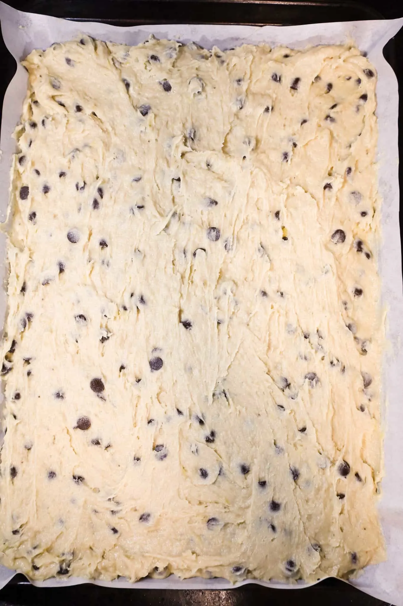 chocolate chip banana bar batter mixture spread in a parchment lined 10 x 15 inch baking sheet