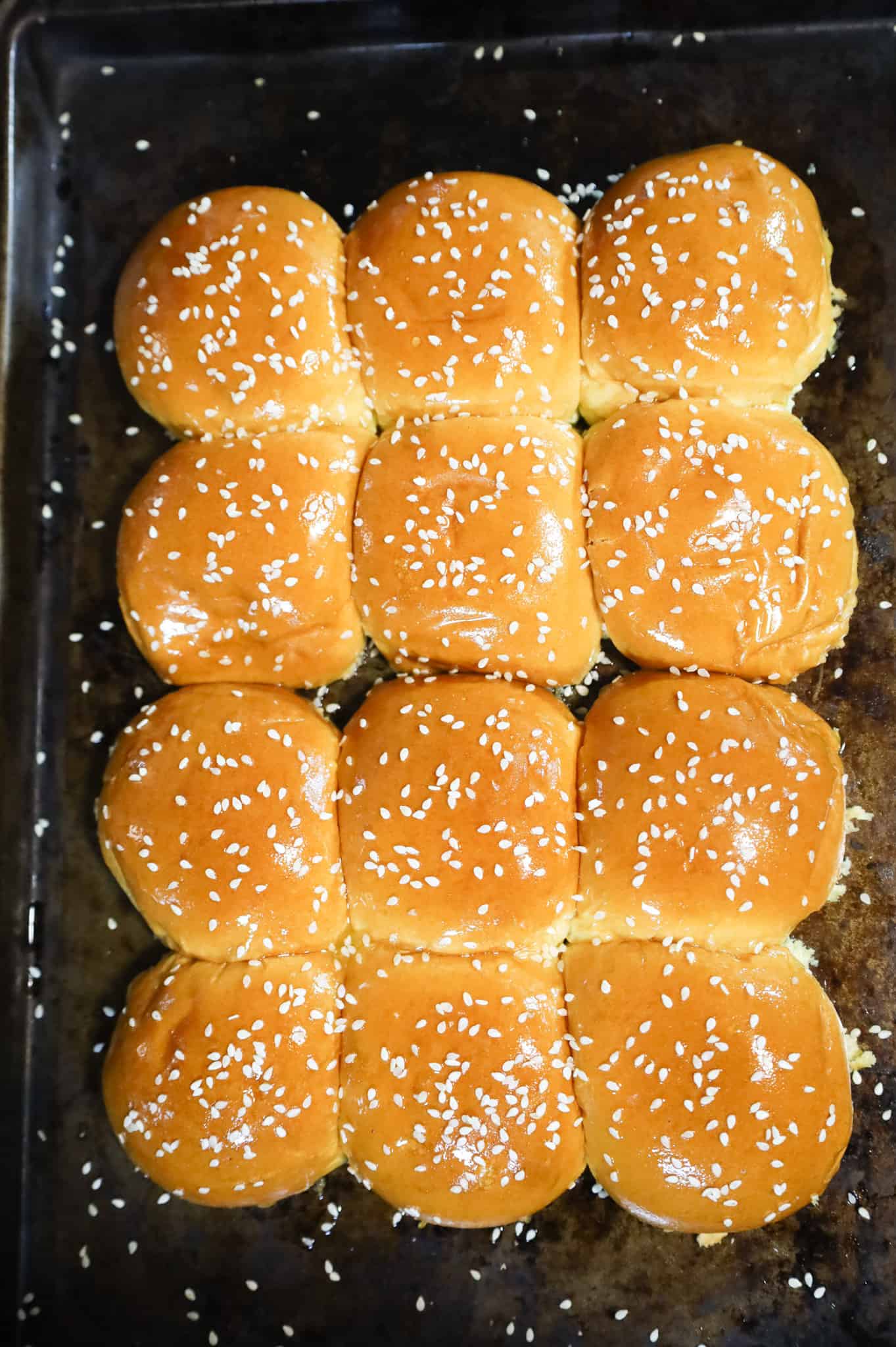 sesame seeds on top of butter brushed buns on a baking sheet