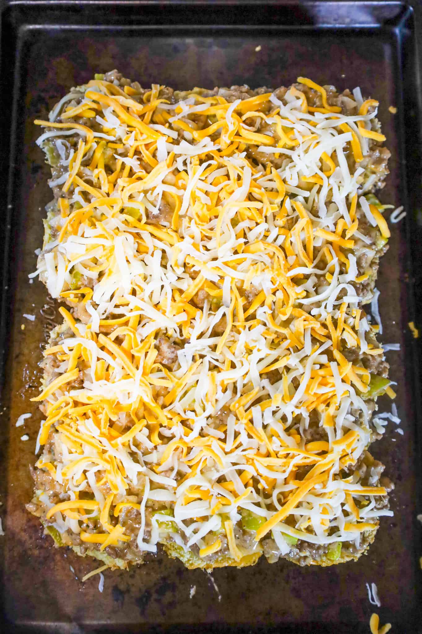 shredded cheddar cheese on top of ground beef mixture on buns on a baking sheet