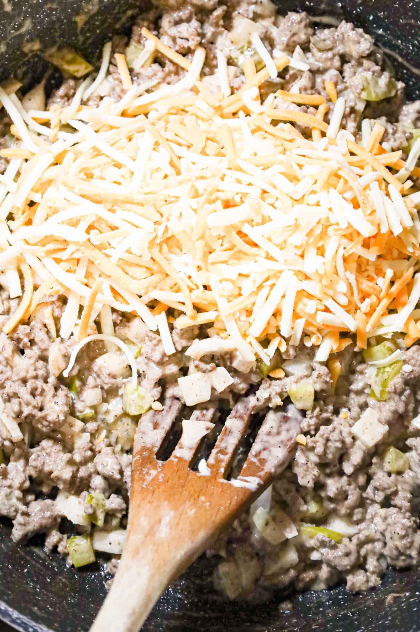 shredded cheddar cheese on top of ground beef mixture in a skillet