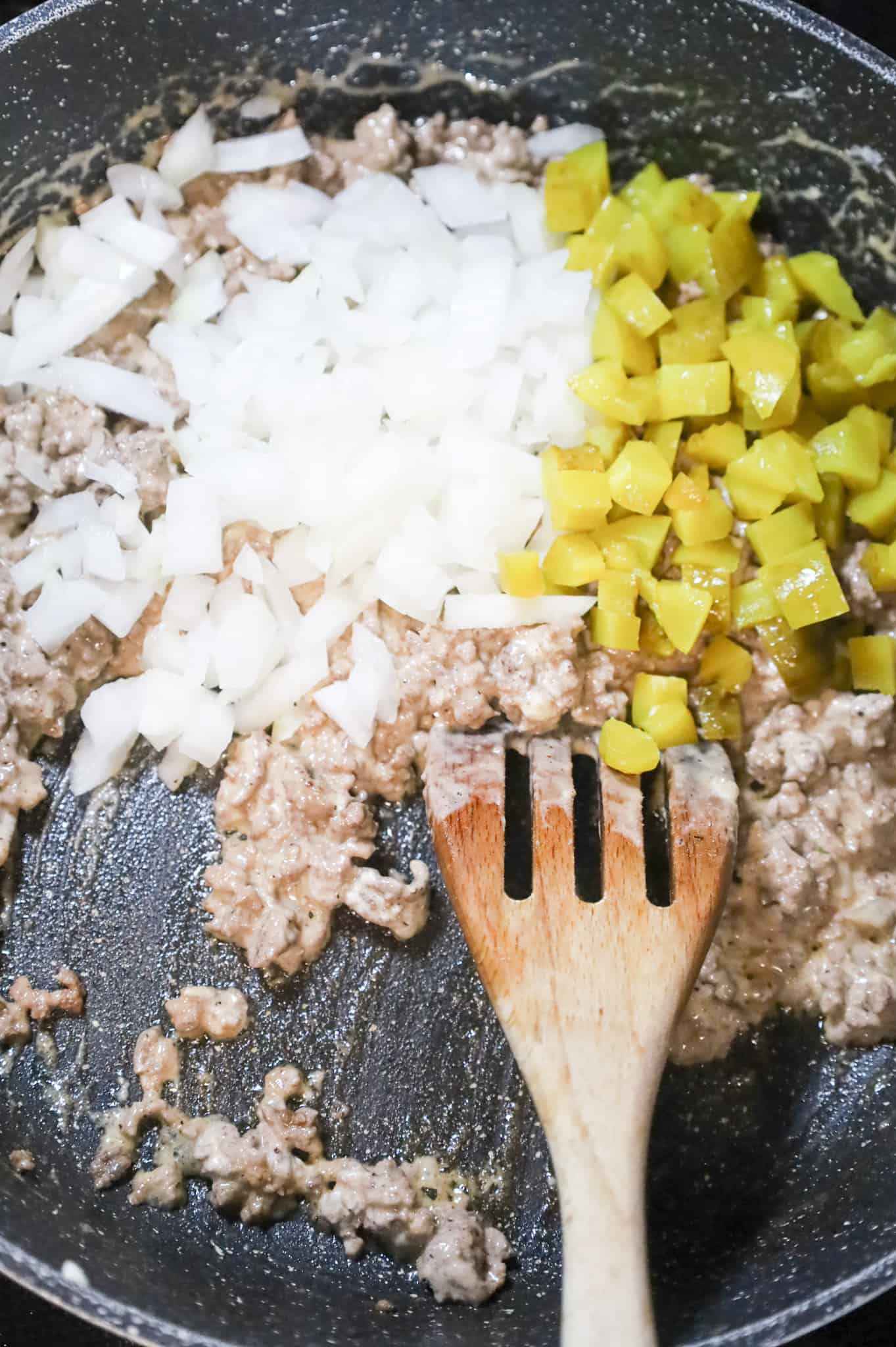 diced onions and diced dill pickles on top of ground beef mixture in a skillet